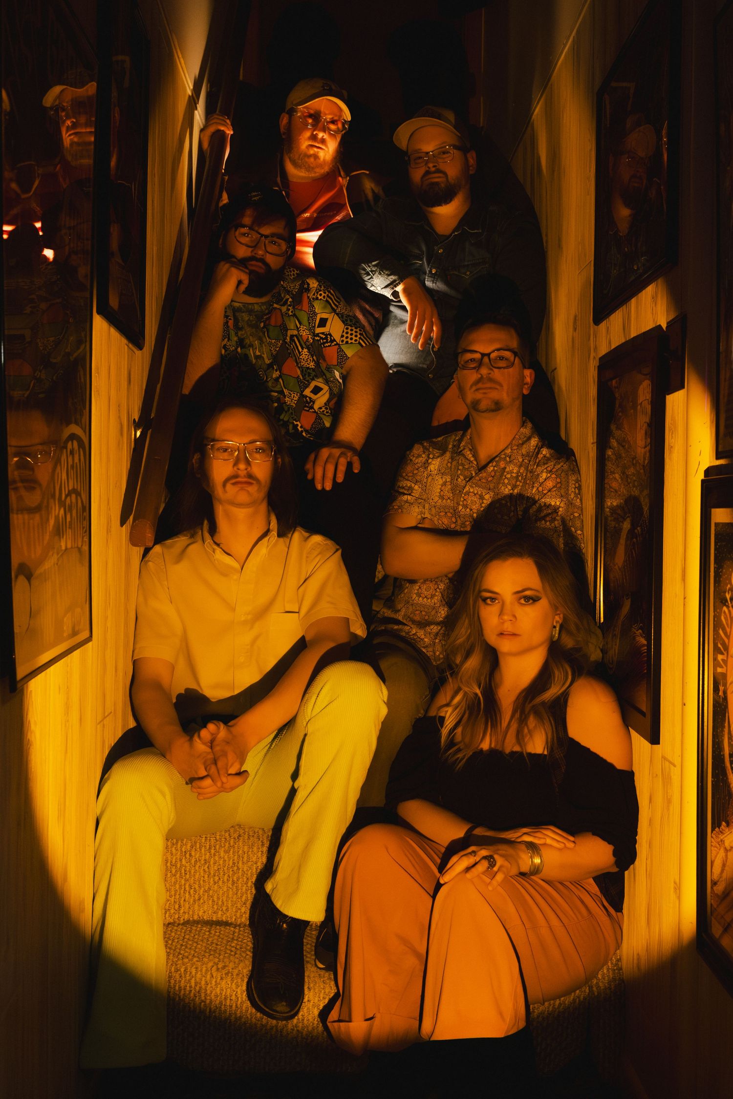 A group of musicians pose on stairs in warm lighting, creating a moody vintage-style promotional photo.