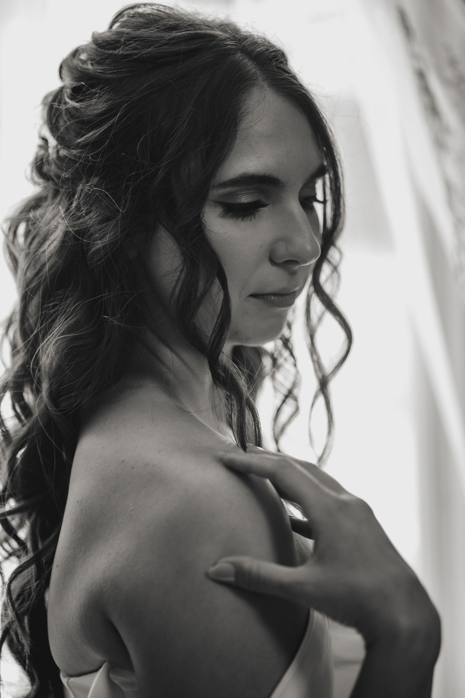 Black and white portrait photo showing person with dark curly hair and bare shoulders in soft natural lighting.