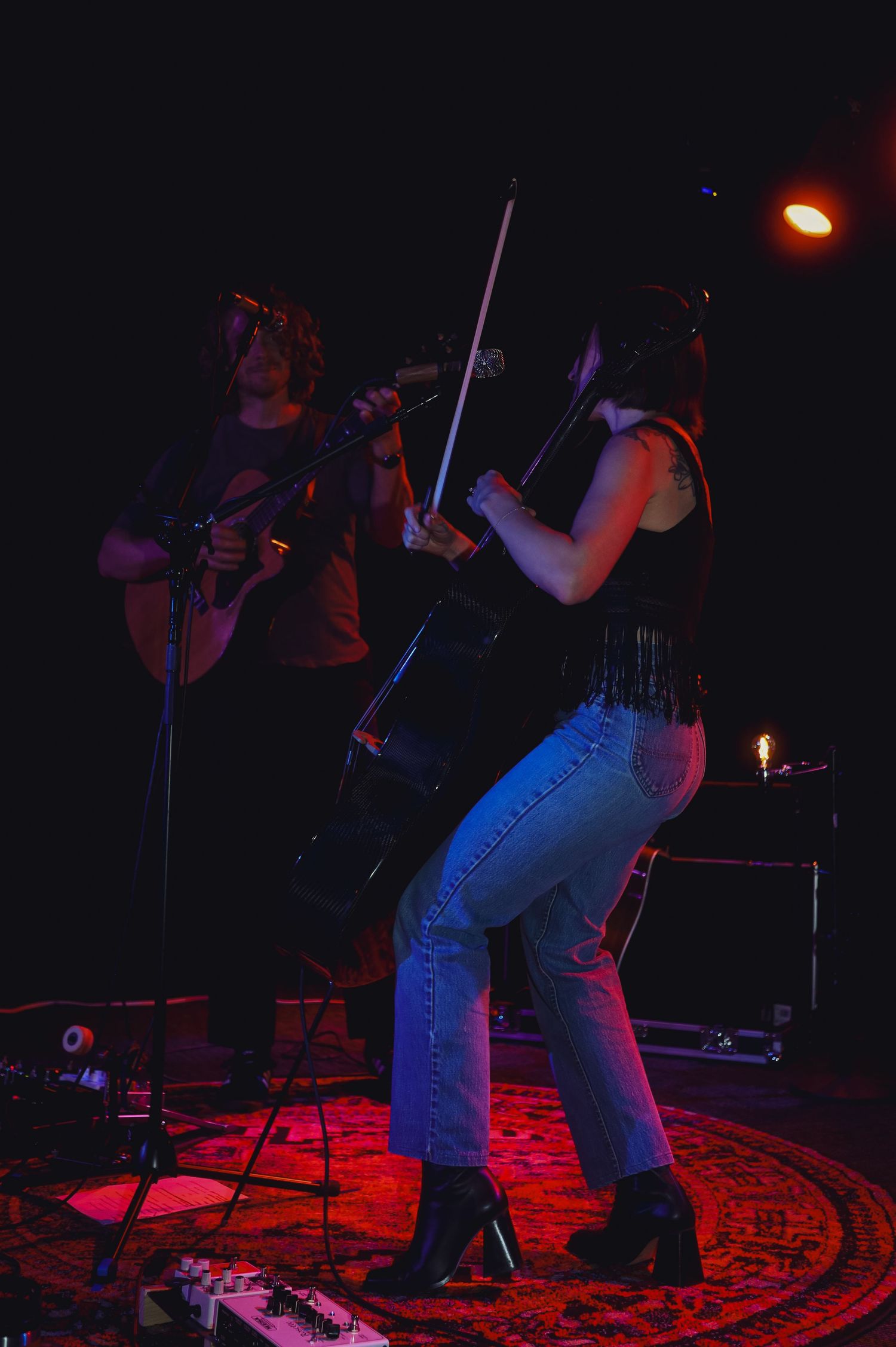 Low-light concert performance with musicians on stage illuminated by red lighting on a patterned carpet.