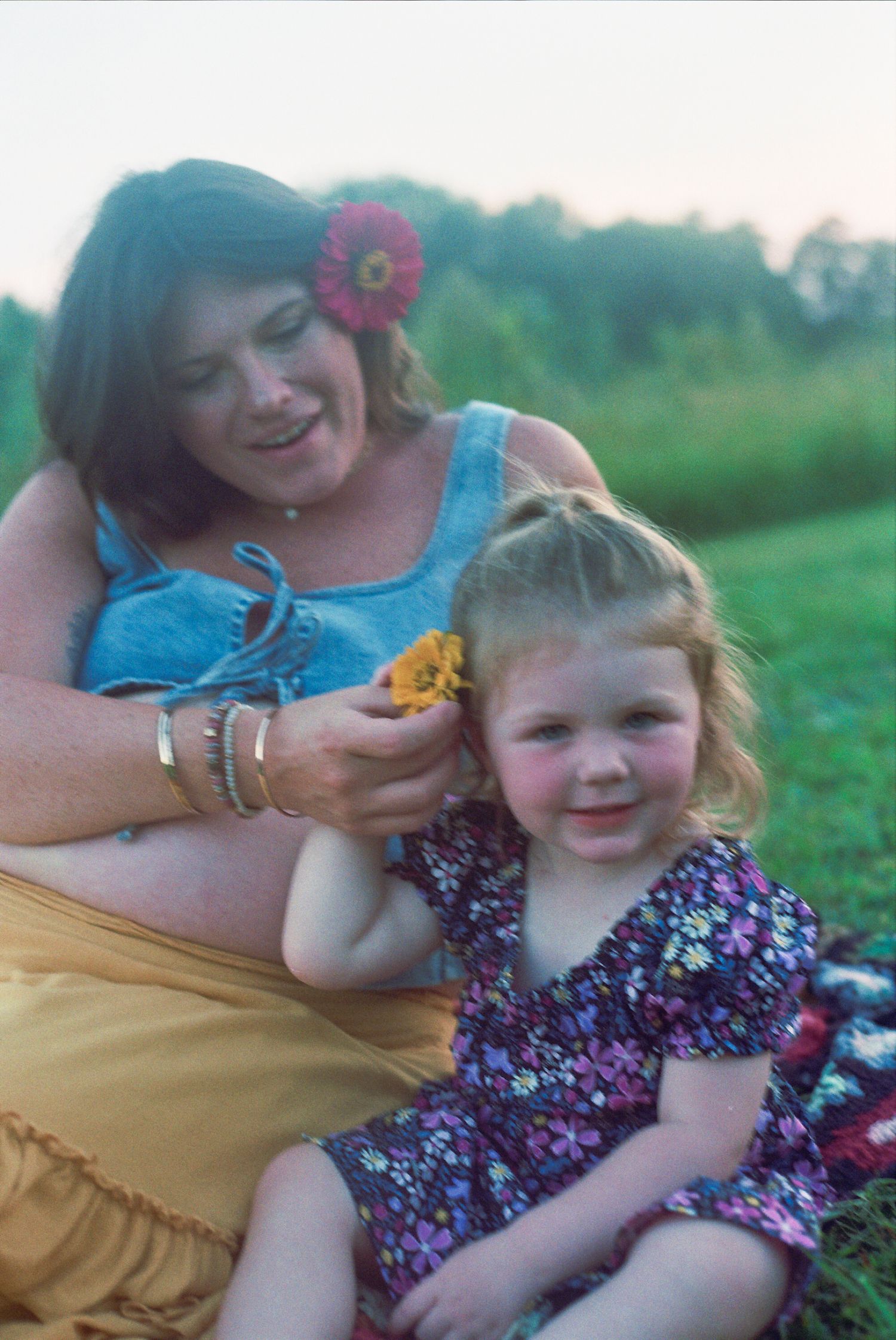 A tender outdoor moment captured on film shows a pair wearing floral accents and bright summer clothing in a grassy field.