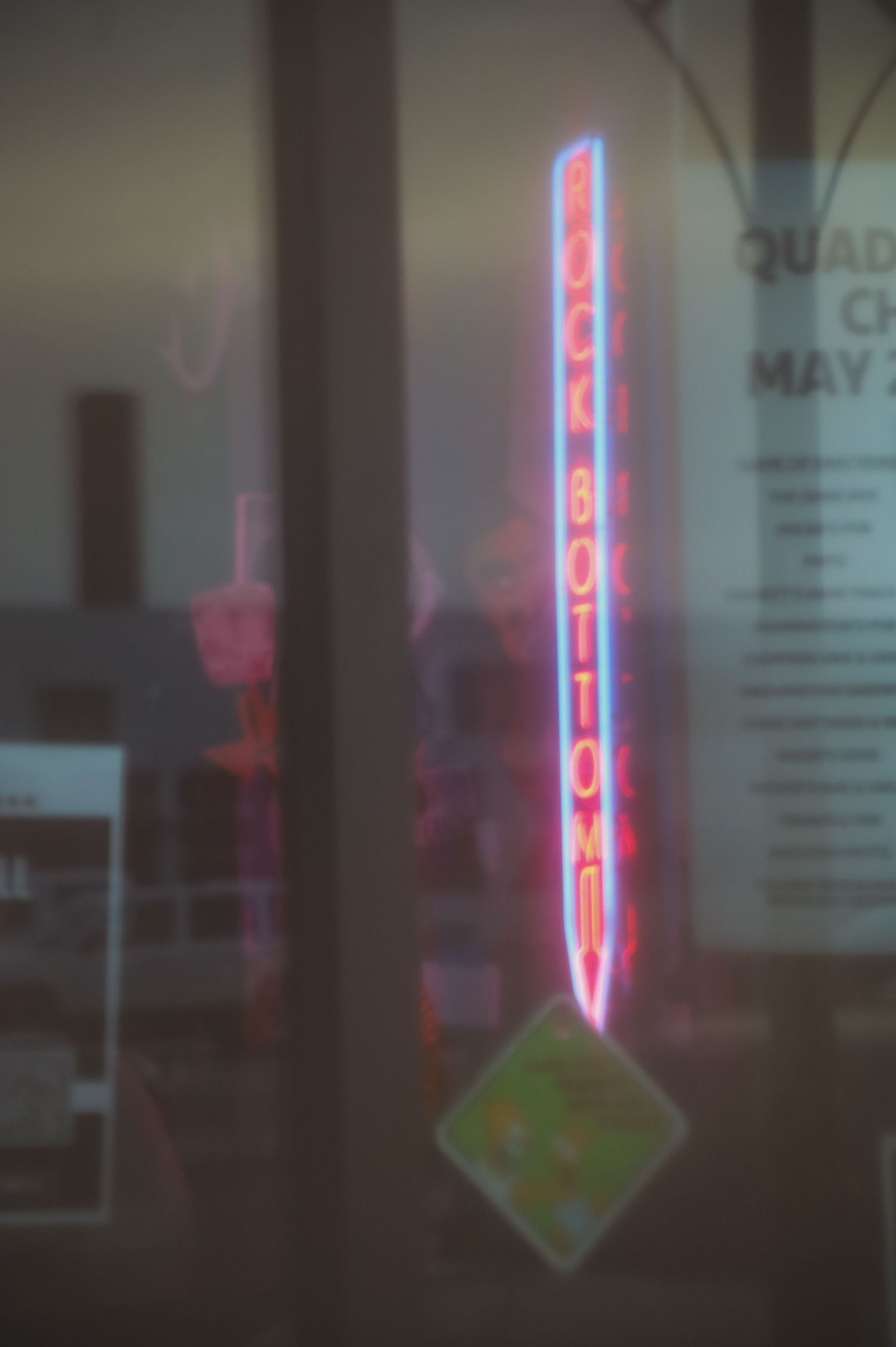 A blurry neon sign with a vertical illuminated arrow shape glows in pink and red against a dark background.