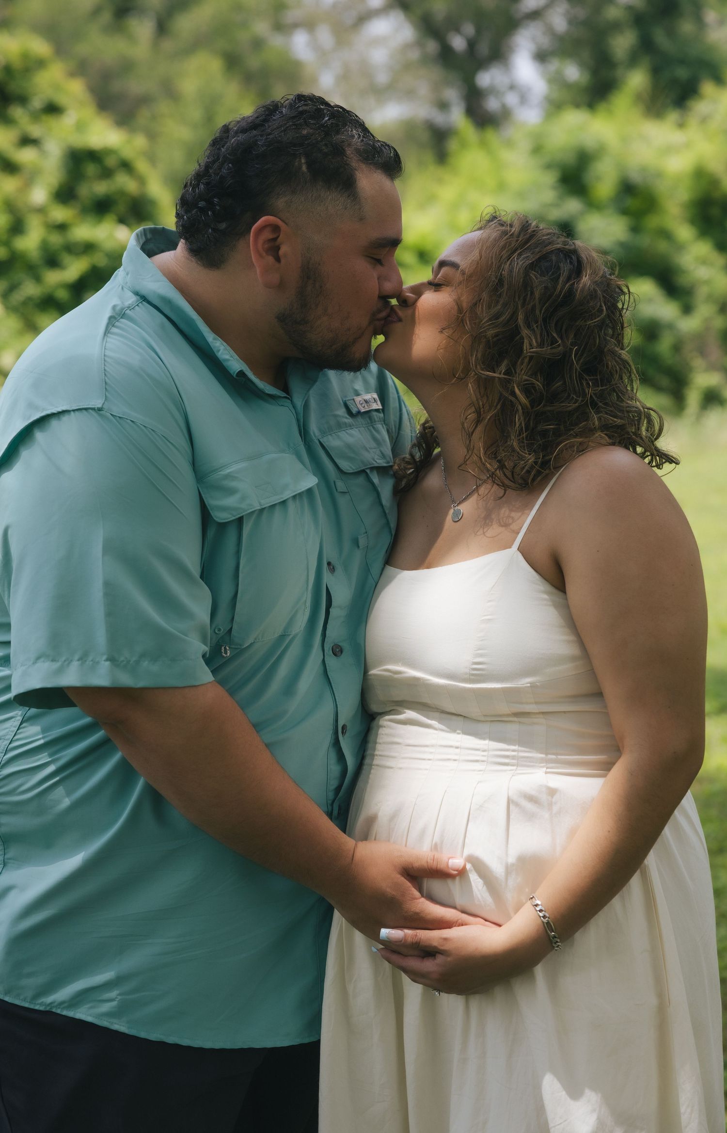 Couple sharing a kiss during a maternity photo shoot outdoors, with the man cradling the pregnant woman's belly.