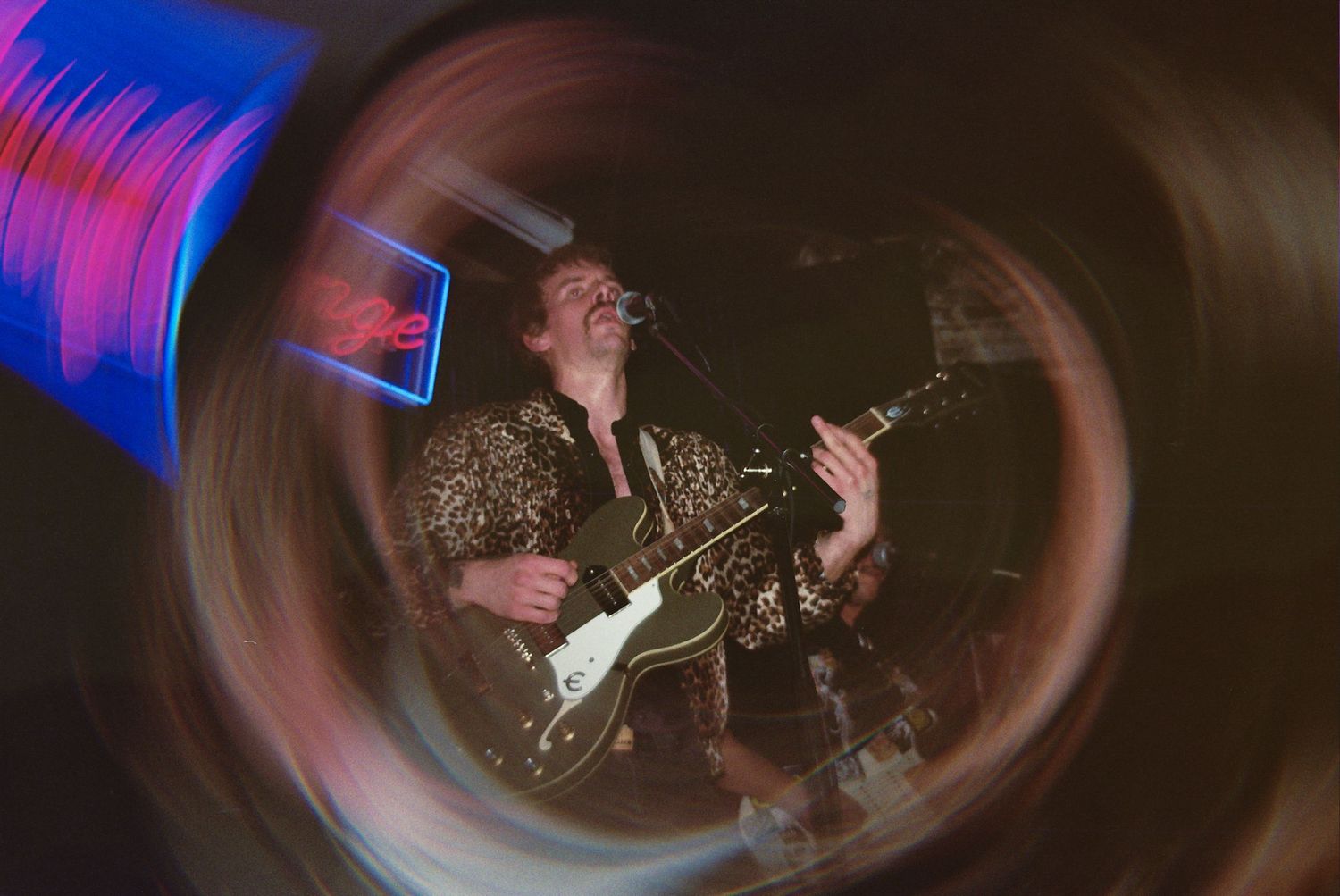 Guitarist performing on stage captured through a swirling vortex lens effect with colorful bokeh lights in a dark venue.