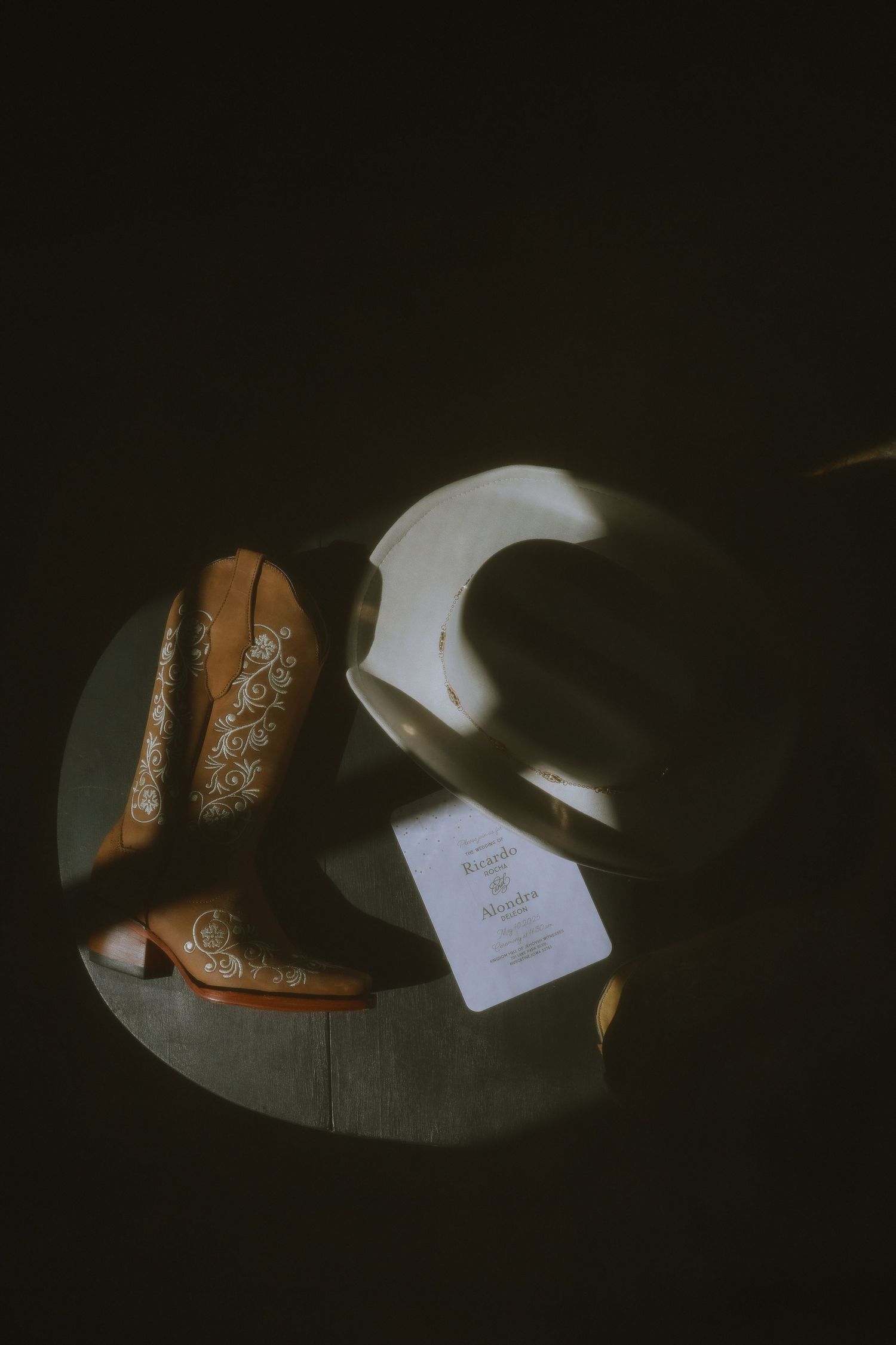 White cowboy boots and hat photographed in dramatic low light with vintage styling on wooden surface.