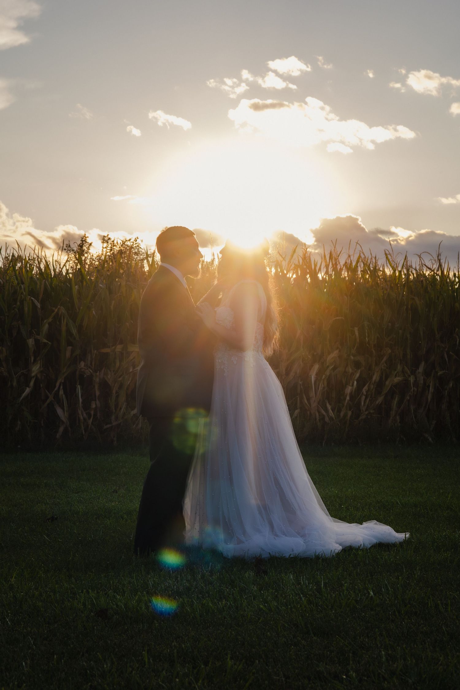 A romantic silhouette of a couple embracing in a field during golden hour sunset with mountains in the background.