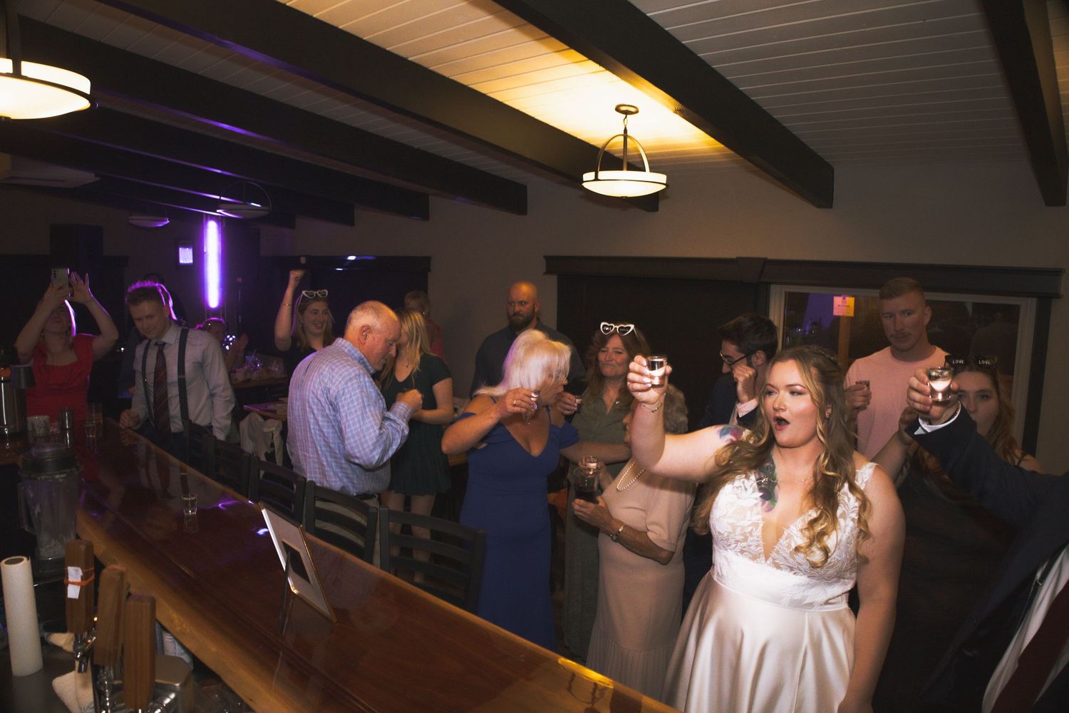 Wedding reception dance party with guests celebrating under moody purple lighting.
