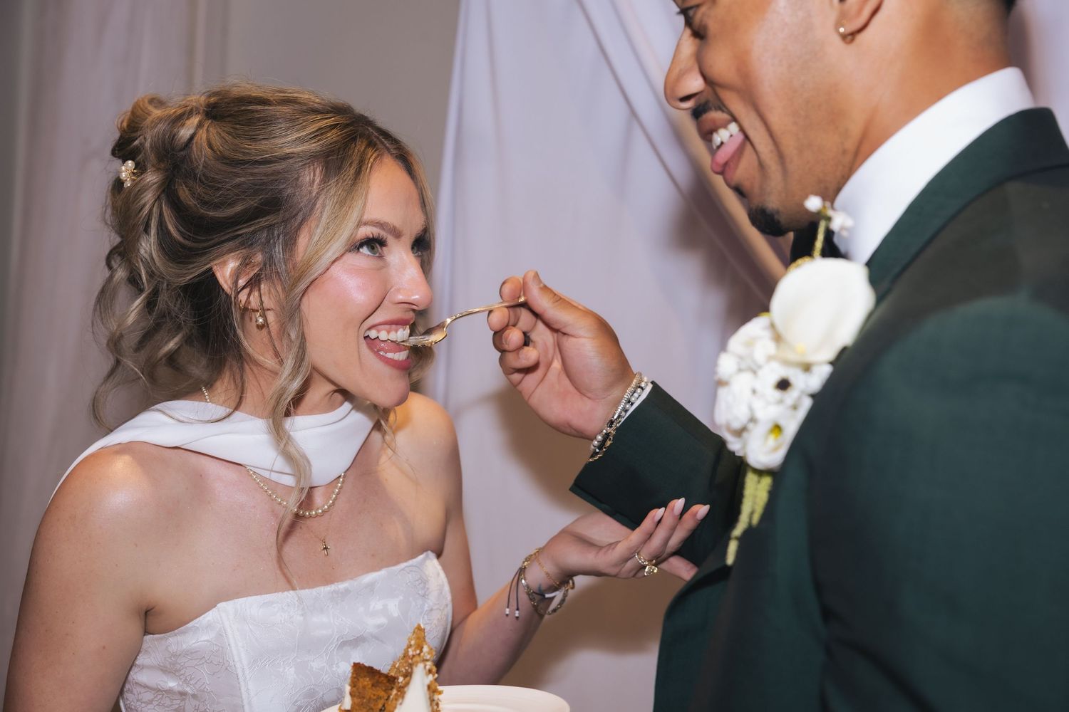 Bride and groom sharing wedding cake, smiling joyfully during reception cake cutting ceremony.