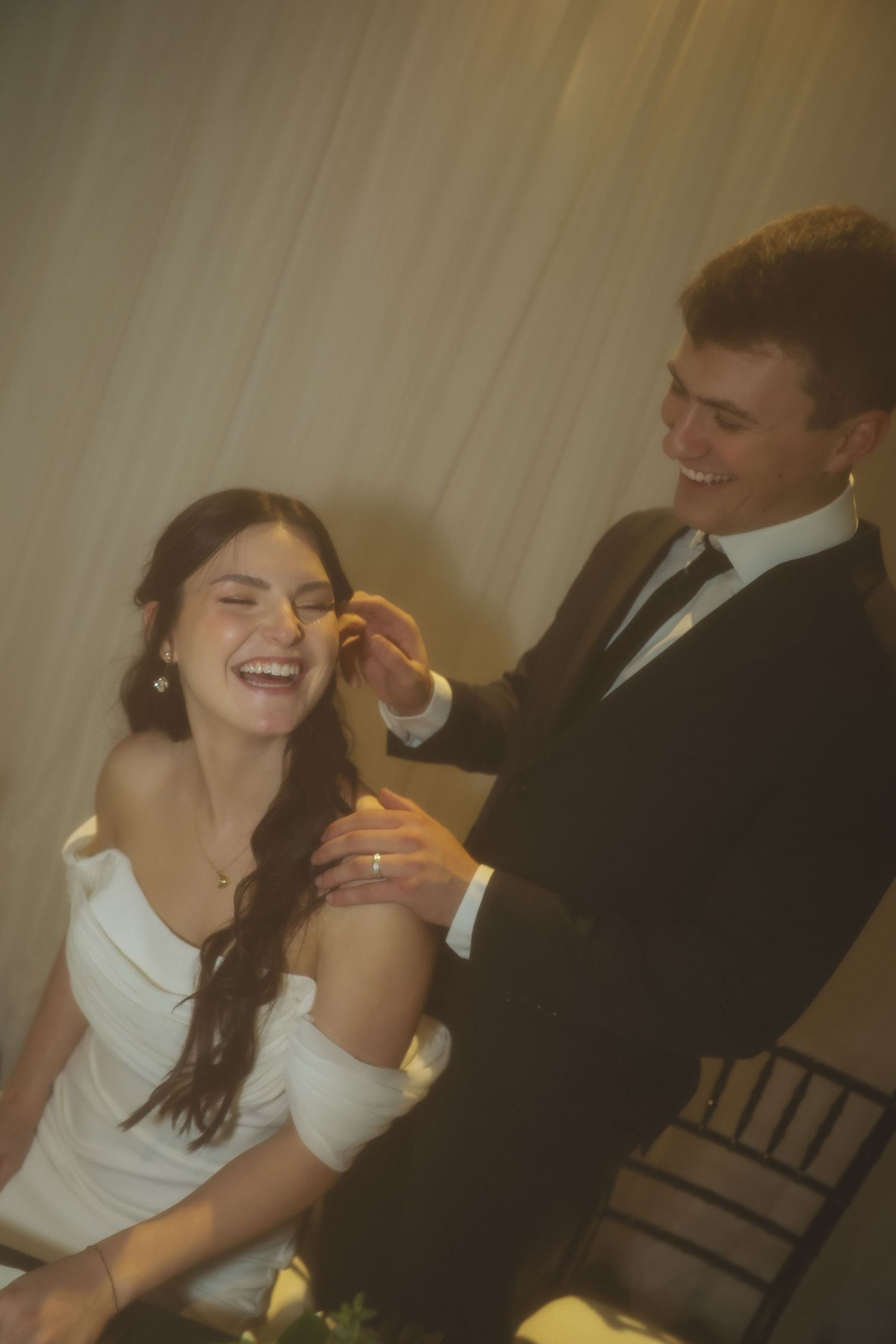 A joyful moment captured between a bride in white and groom in black suit during their wedding reception.