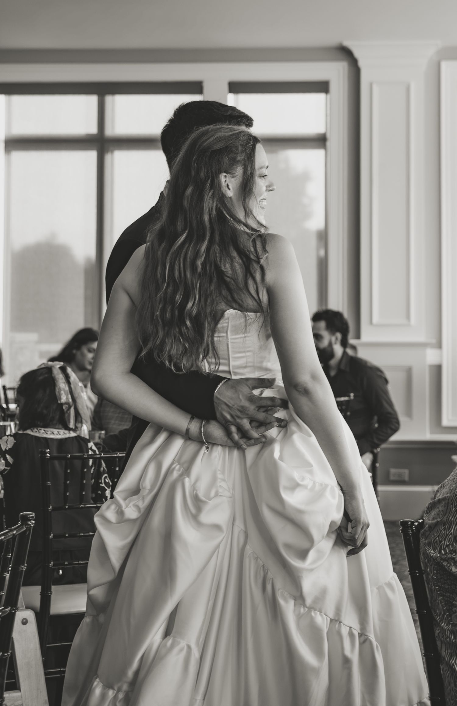 Black and white photo of a bride in a white gown being embraced by groom at a wedding reception.
