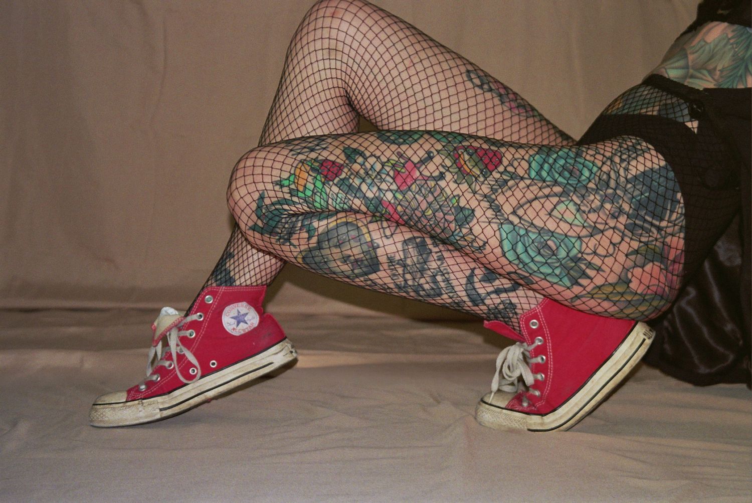 Person wearing red Converse sneakers and fishnet stockings with colorful tattoos on legs.