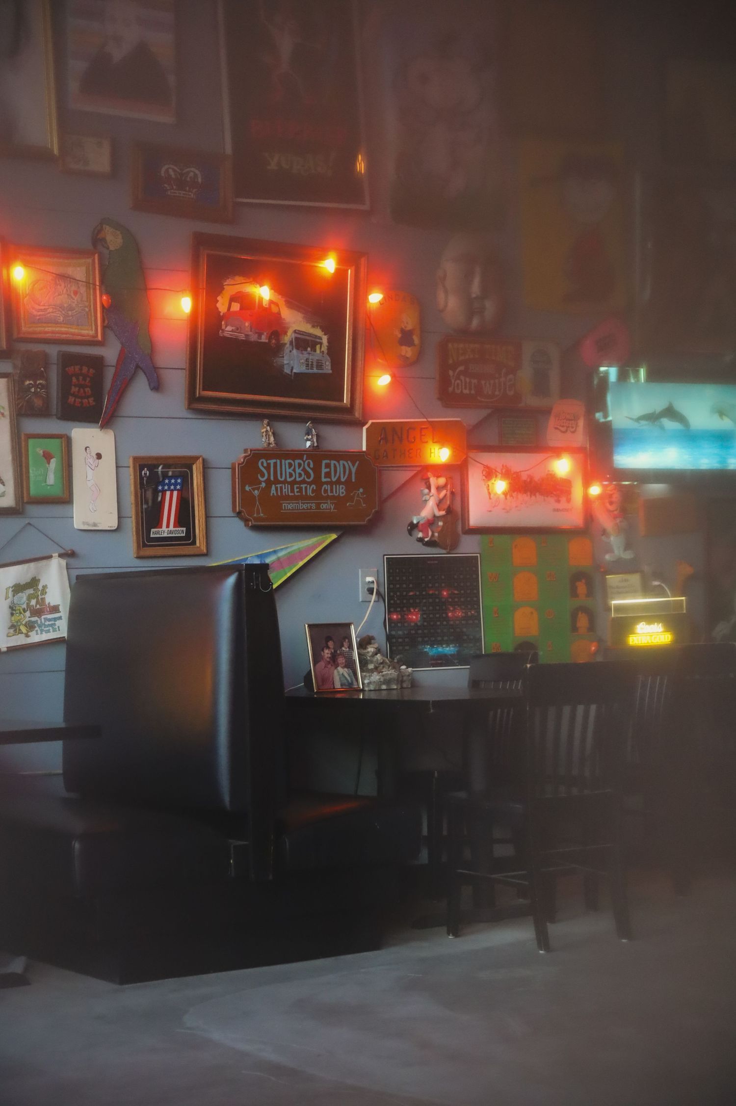Dark interior of a bar or restaurant with neon lights glowing on the walls and empty leather booth seating.