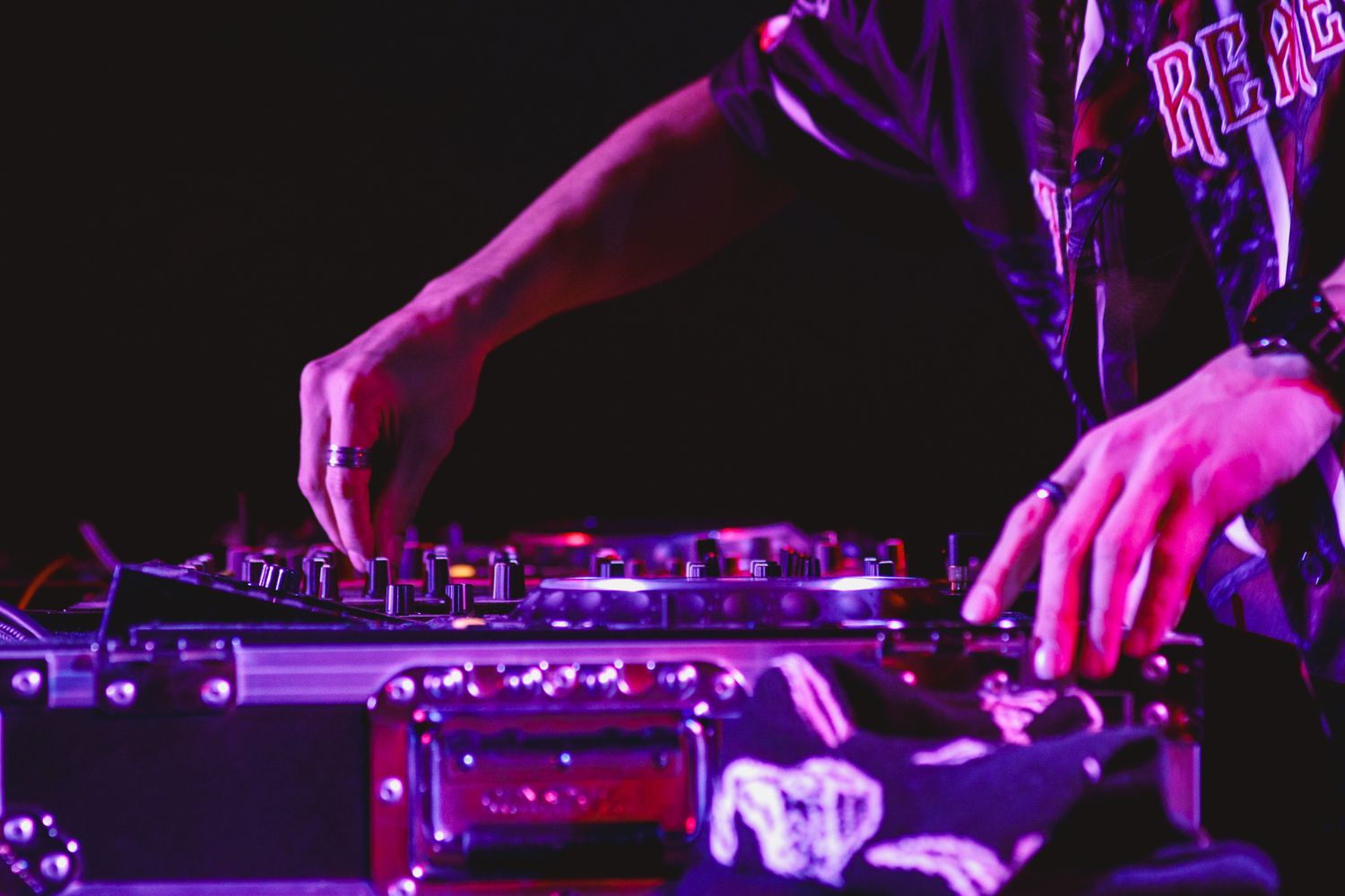 DJ hands working on turntables and mixer equipment illuminated by purple stage lighting at a nightclub performance.