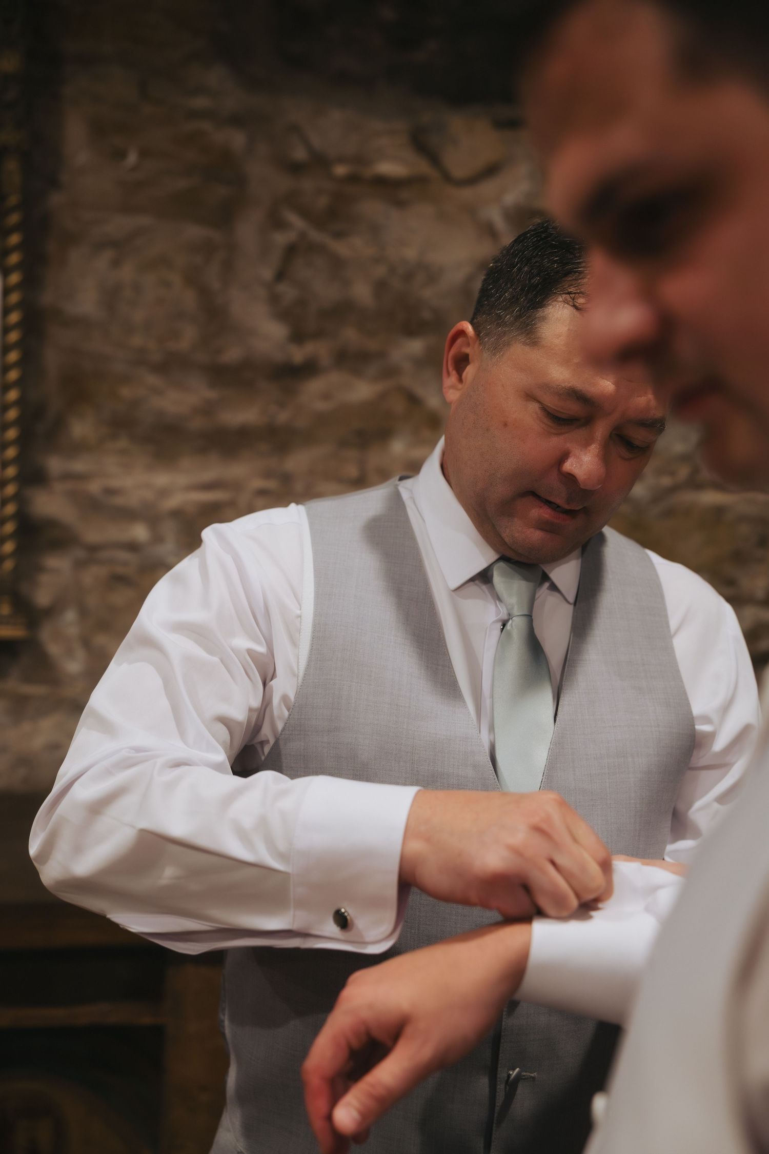 A person wearing a light gray vest and tie signs papers at a formal event or ceremony.
