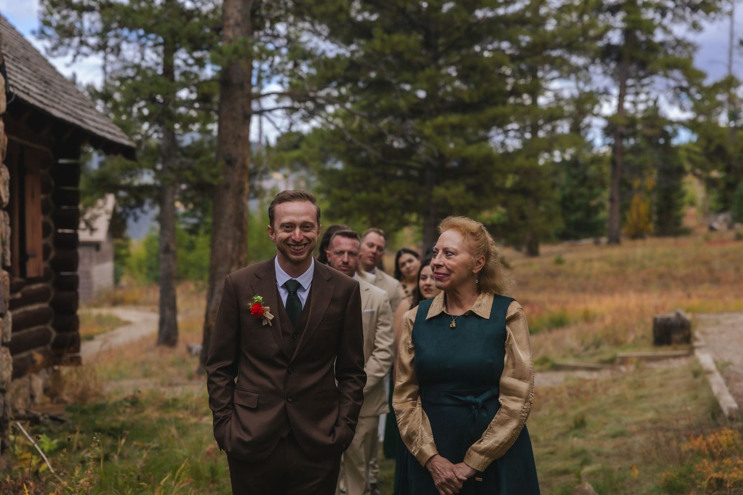 Wedding party laughing and enjoying a candid moment together in a rustic outdoor setting with pine trees.