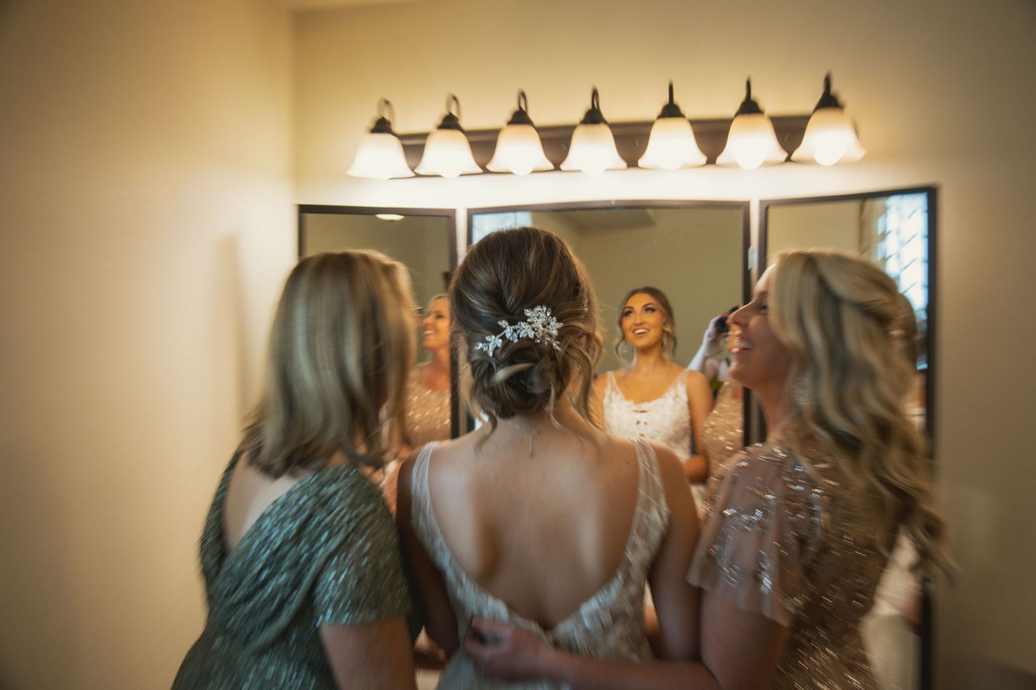Getting ready scene reflected in a bathroom mirror with vanity lights.
