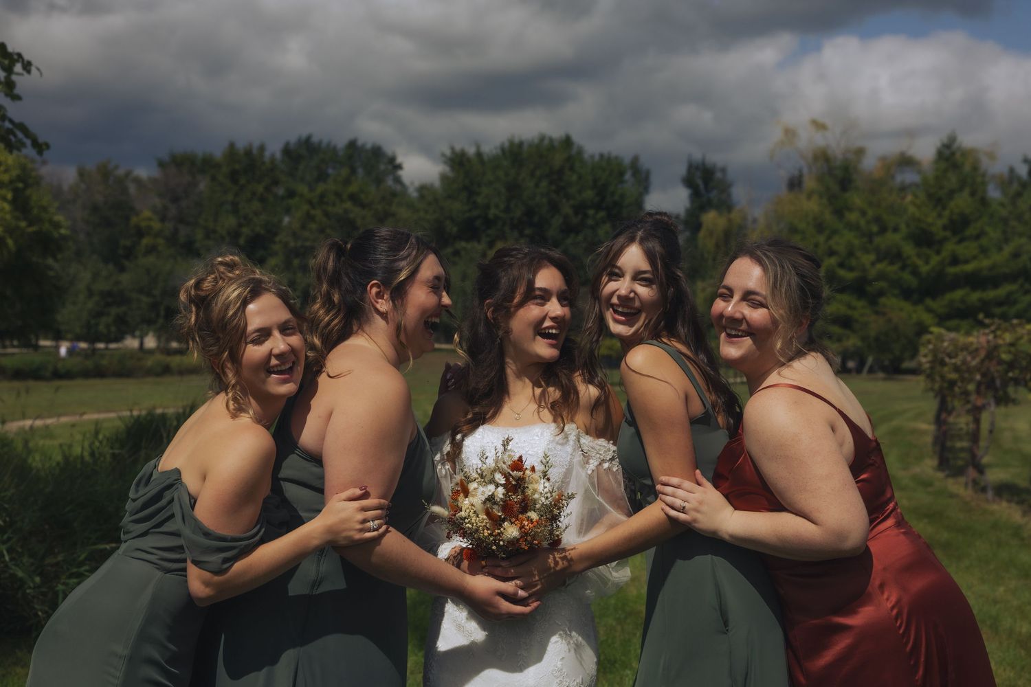 A group of people share joyful laughter together outdoors on a cloudy day in a vineyard setting.