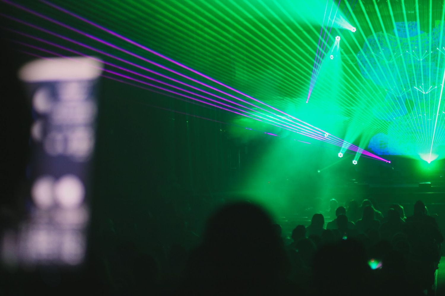 Concert venue illuminated with bright green laser beams creating dramatic lighting effects during a performance.