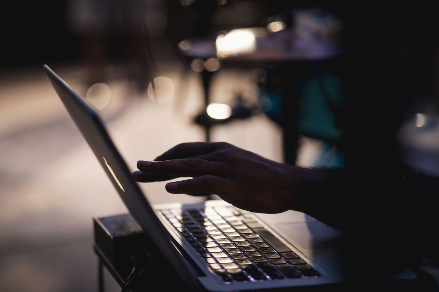 Silhouetted hands typing on a laptop keyboard in low ambient lighting.