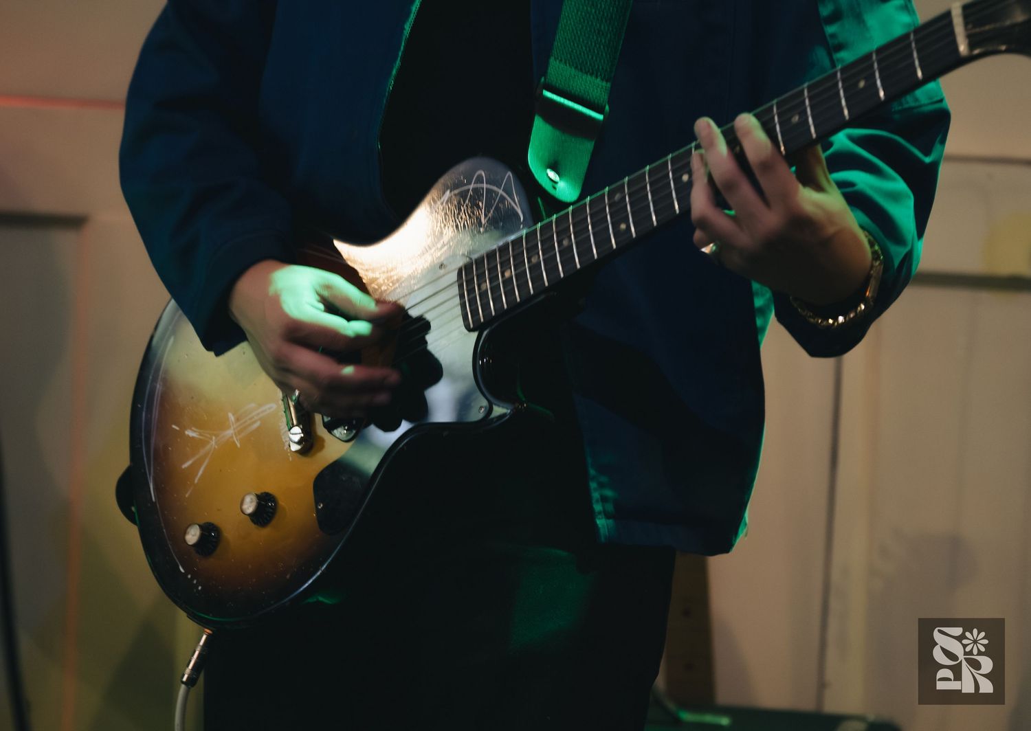 Musician playing a vintage sunburst electric guitar with a green strap during a live performance.