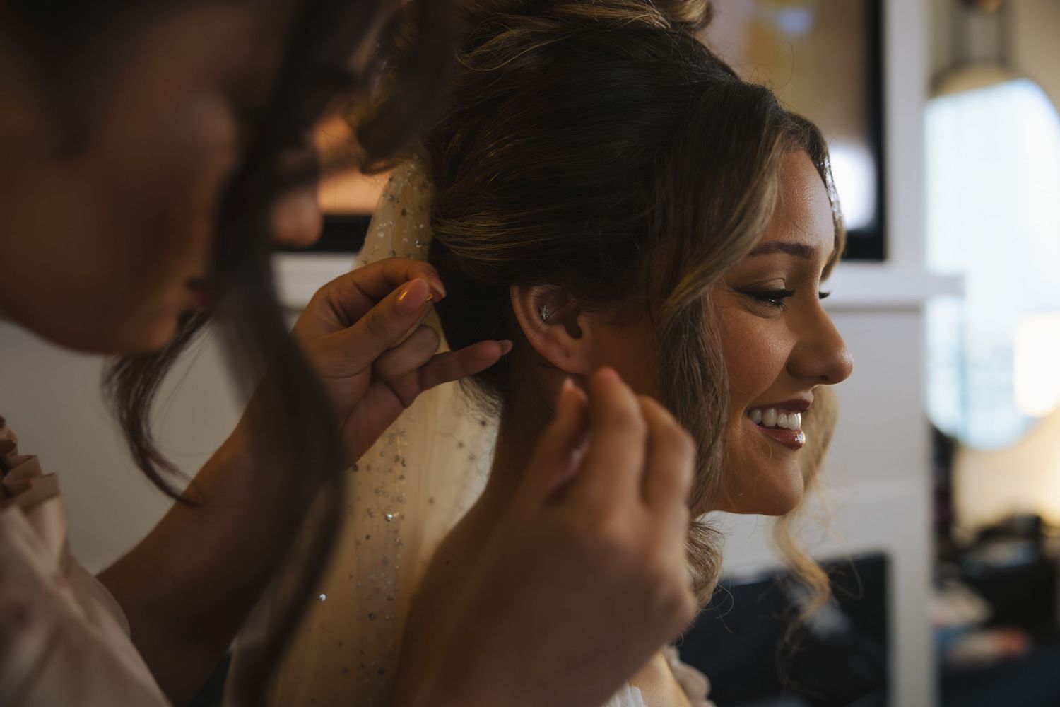 A candid moment at a wedding where a bride is being helped with final touches to her hair and makeup.