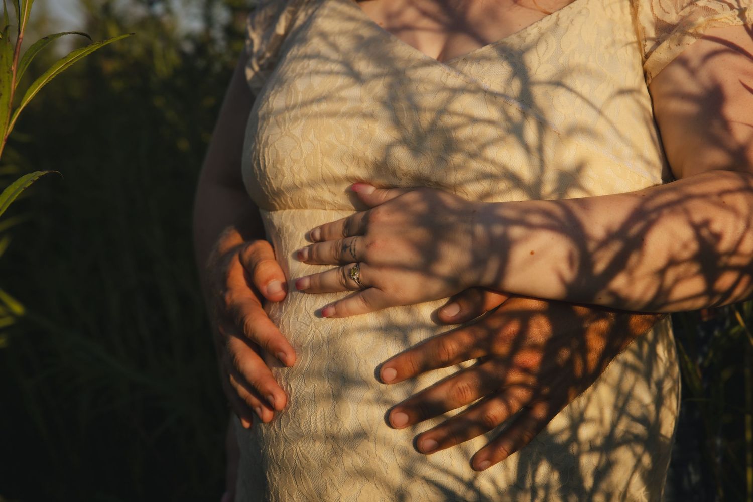 Beautiful shadows from tree branches cast across a white dress and hands at golden hour.