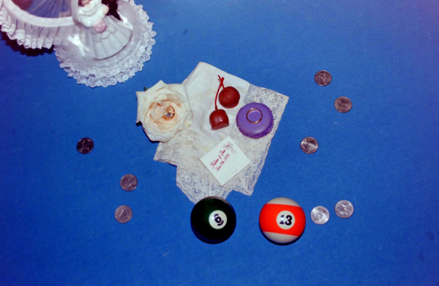 Blue surface with billiard balls, coins, lace fabric, dried rose, and small trinkets arranged in a flat lay composition.