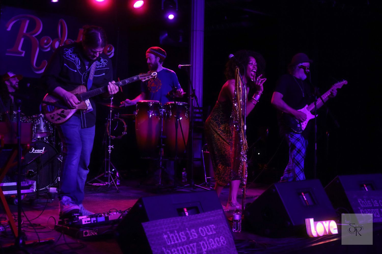 Musicians perform on stage in a dimly lit venue with purple lighting creating a moody concert atmosphere.