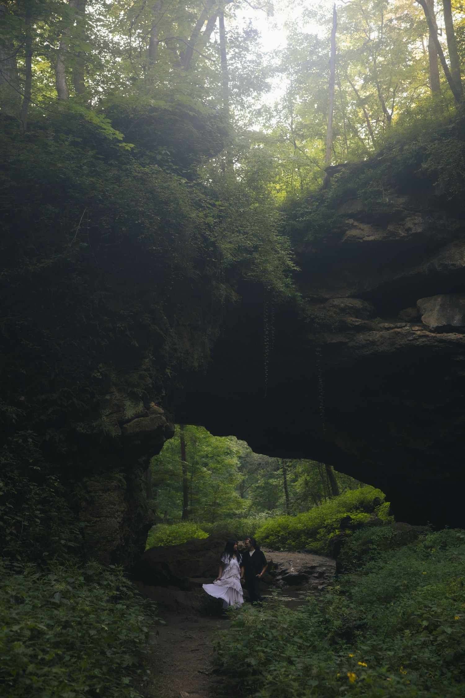 Misty stone archway in a lush green forest creates a natural tunnel through moss-covered rock formations.