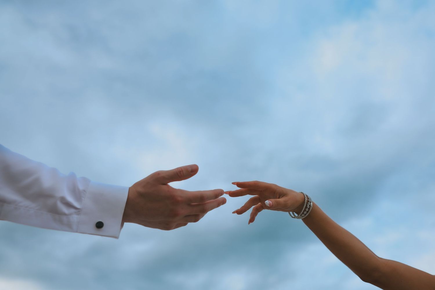 A row of hands with interlinked fingers creating a human chain against a cloudy sky background.