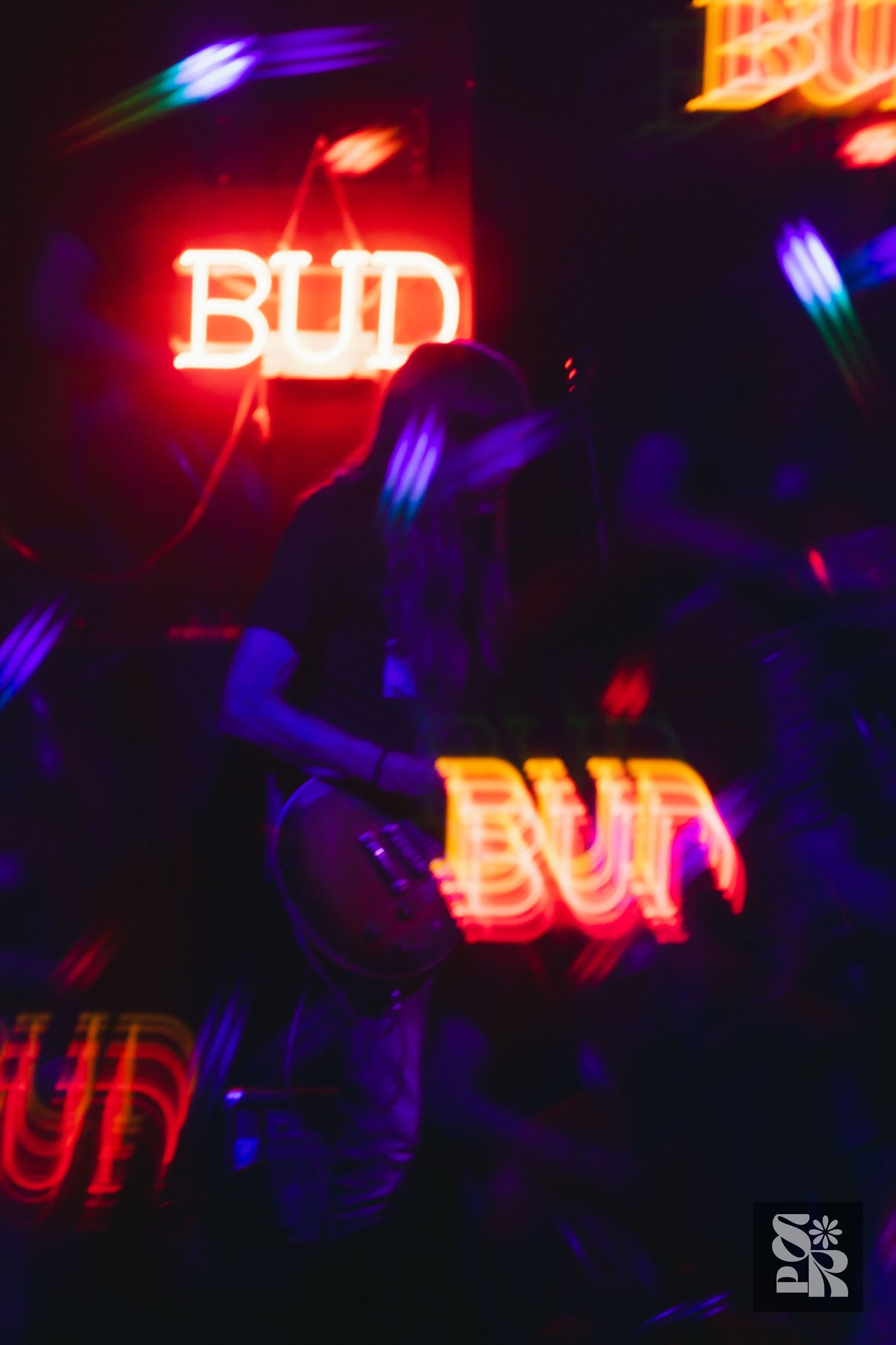 Musician performing on stage in dark club with glowing red BUD neon signs creating atmospheric light effects.