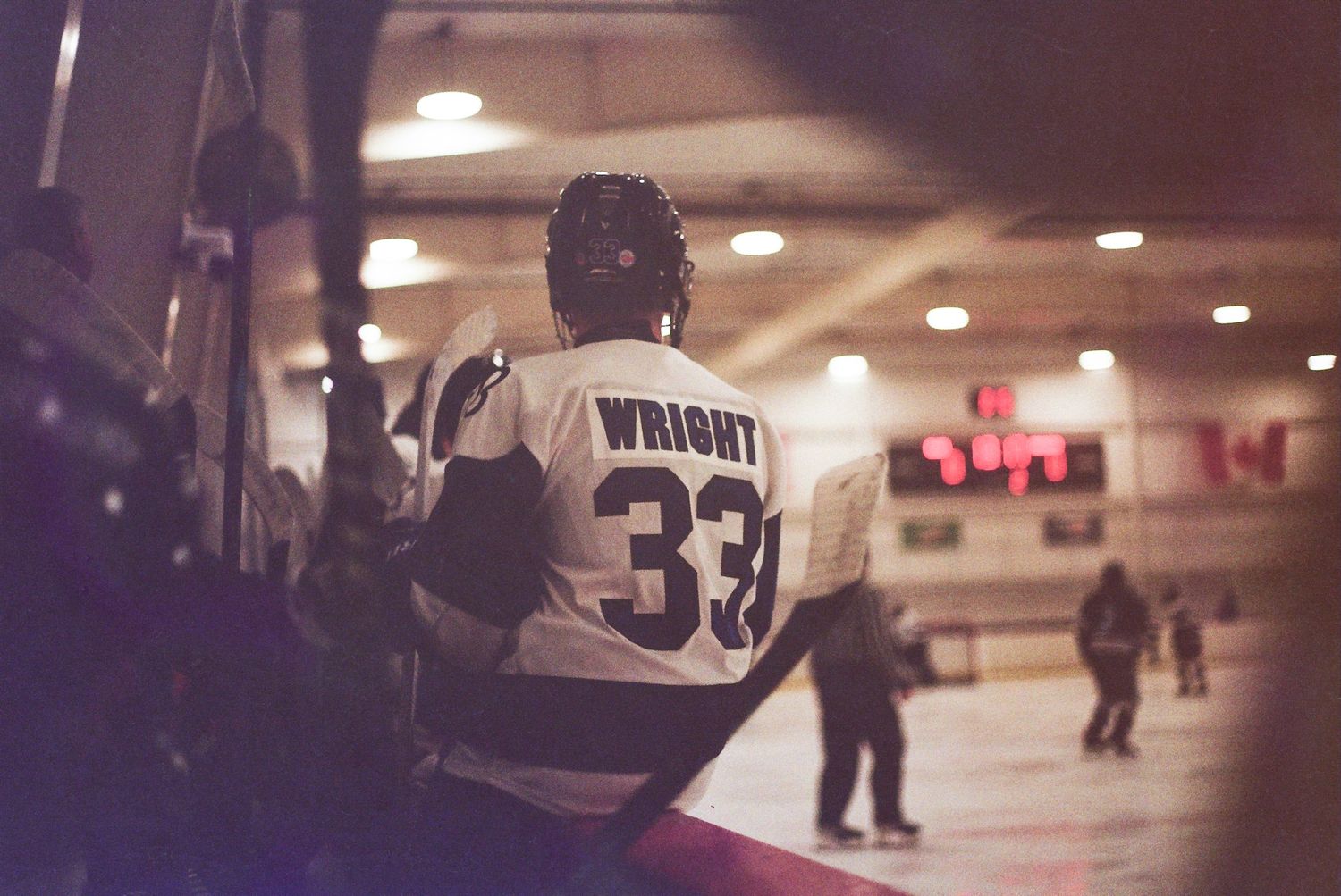 Hockey player wearing Wright #33 jersey stands at the boards during an indoor ice hockey game.