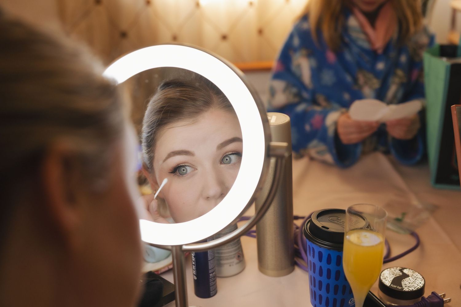 Woman applying eye makeup while looking into a round LED vanity mirror on a dressing table.