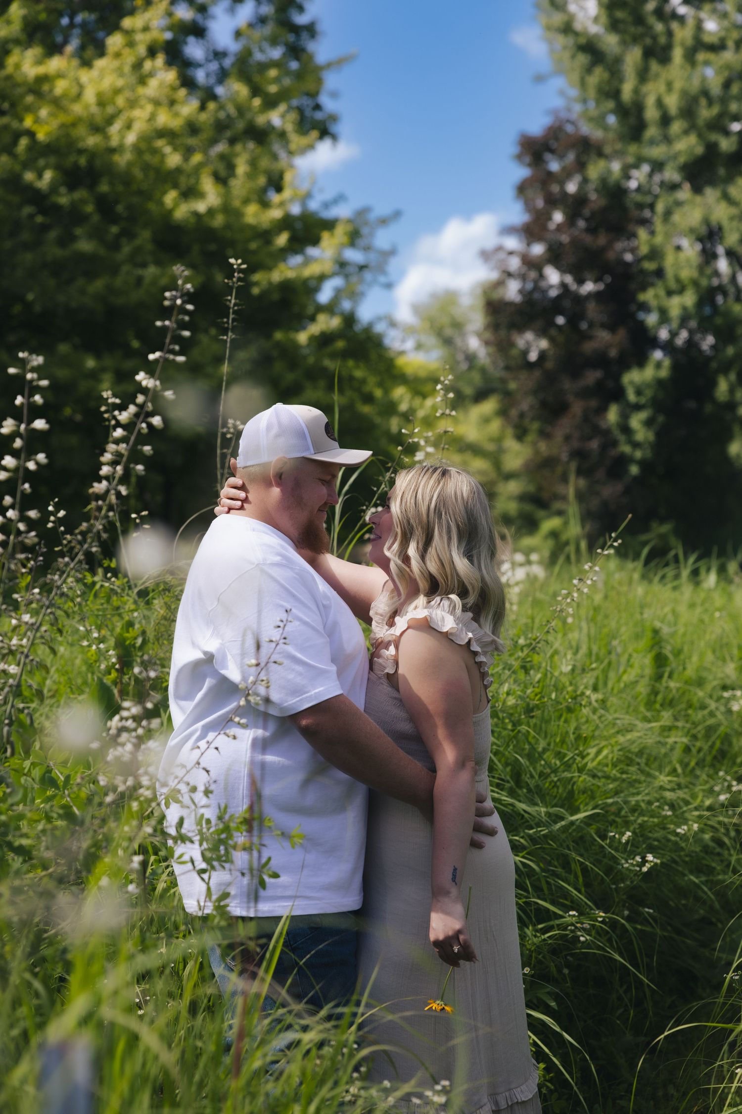 Couple embracing in a lush green meadow with wildflowers on a sunny day.