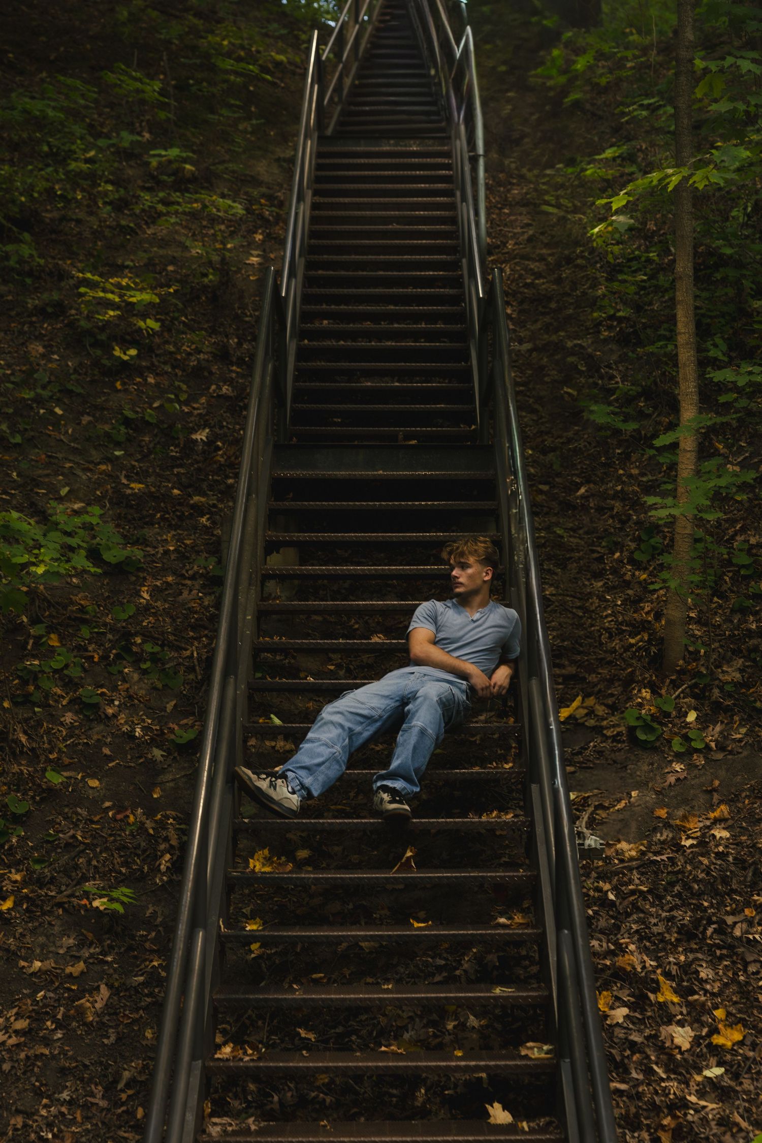 Long metal staircase in wooded area with scattered autumn leaves on the ground.