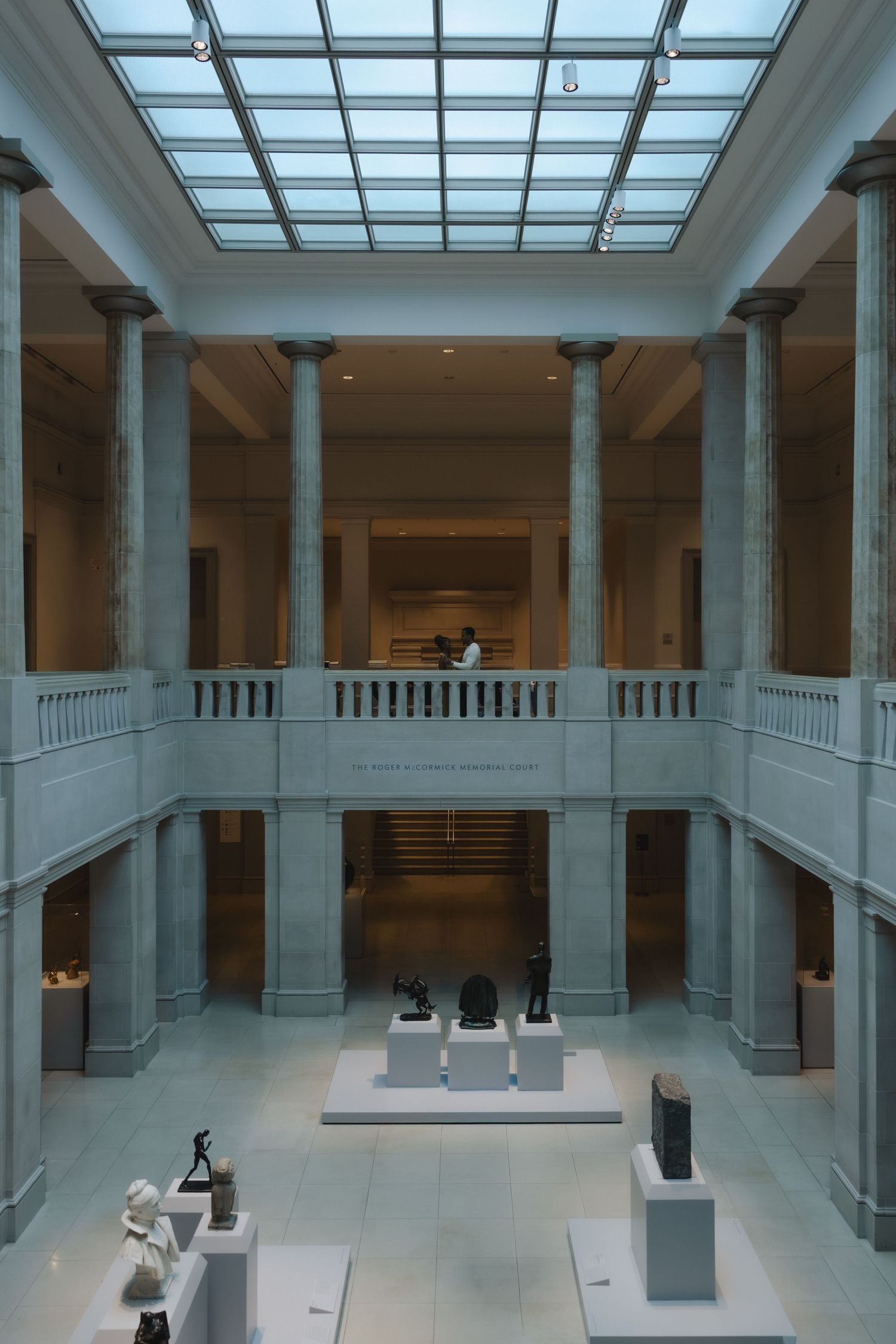 Grand museum atrium with classical columns, skylight ceiling, and sculpture displays on two levels.