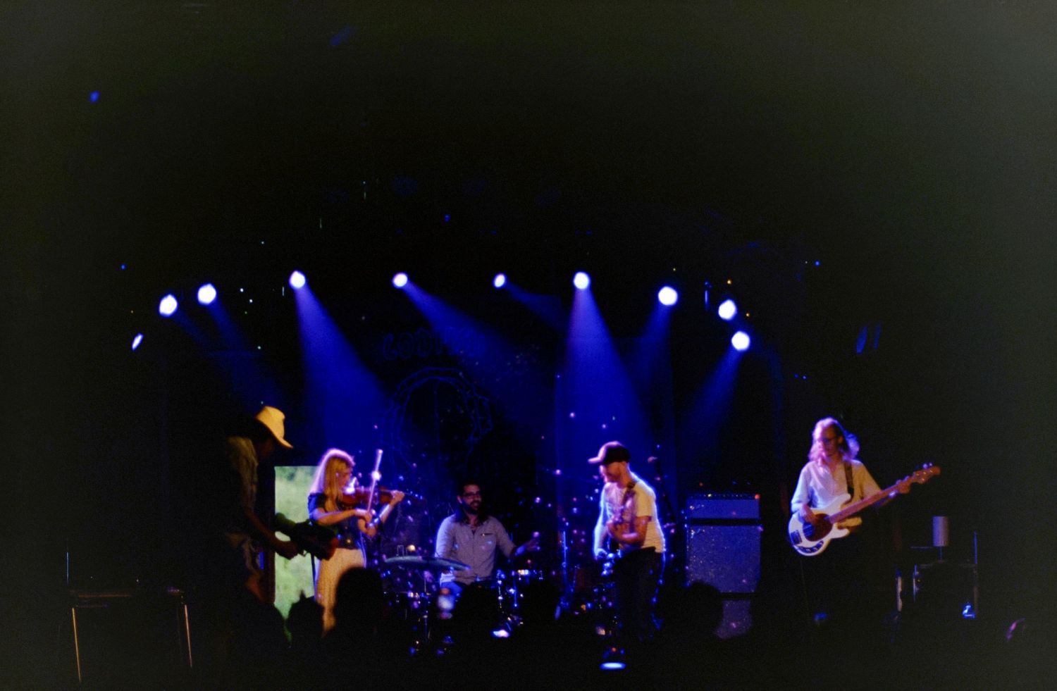A rock band performs on a dimly lit stage with blue spotlights during a live concert.