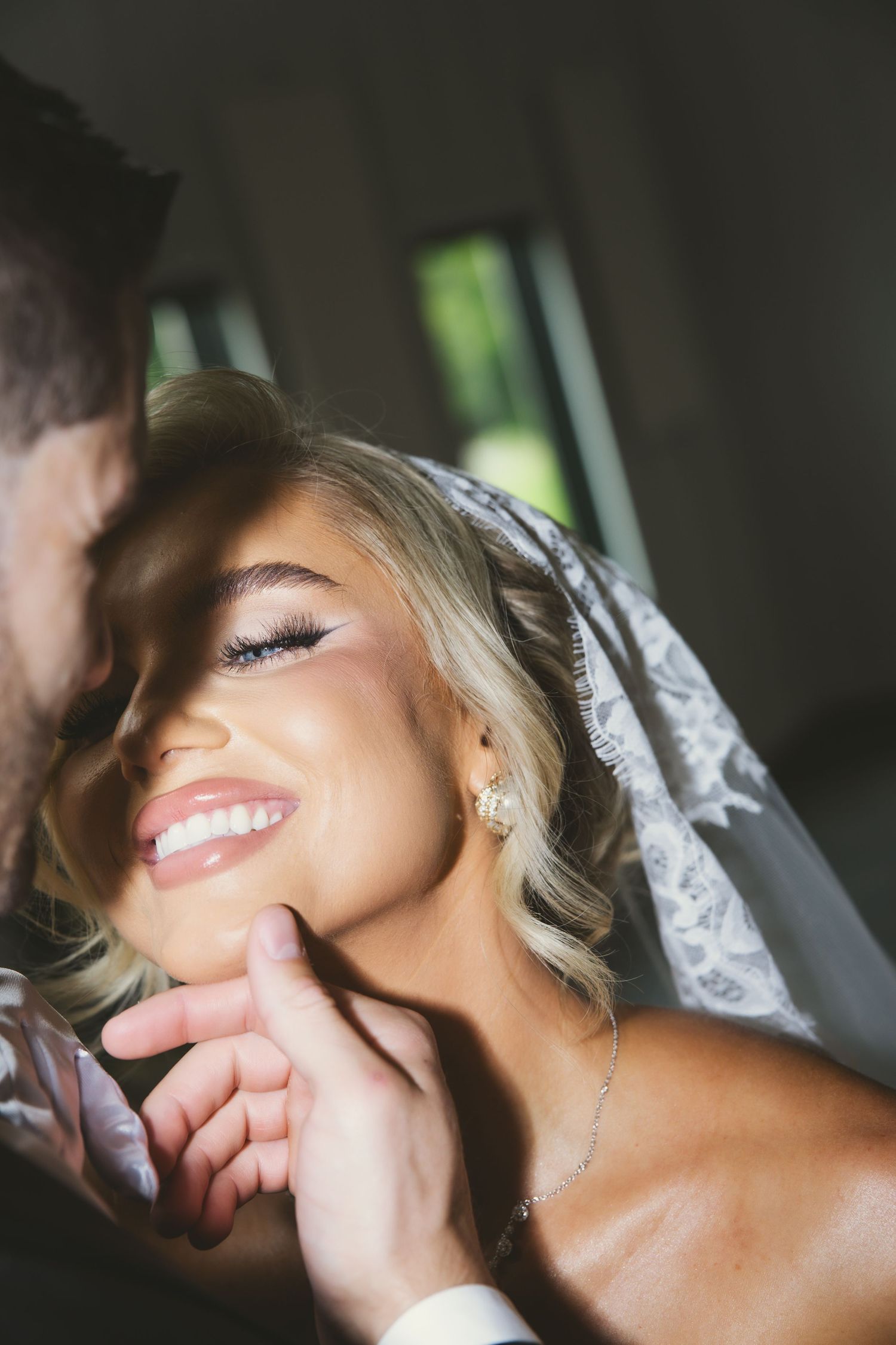 Close up photo captures a tender intimate moment and joyful smile through a delicate white wedding veil.