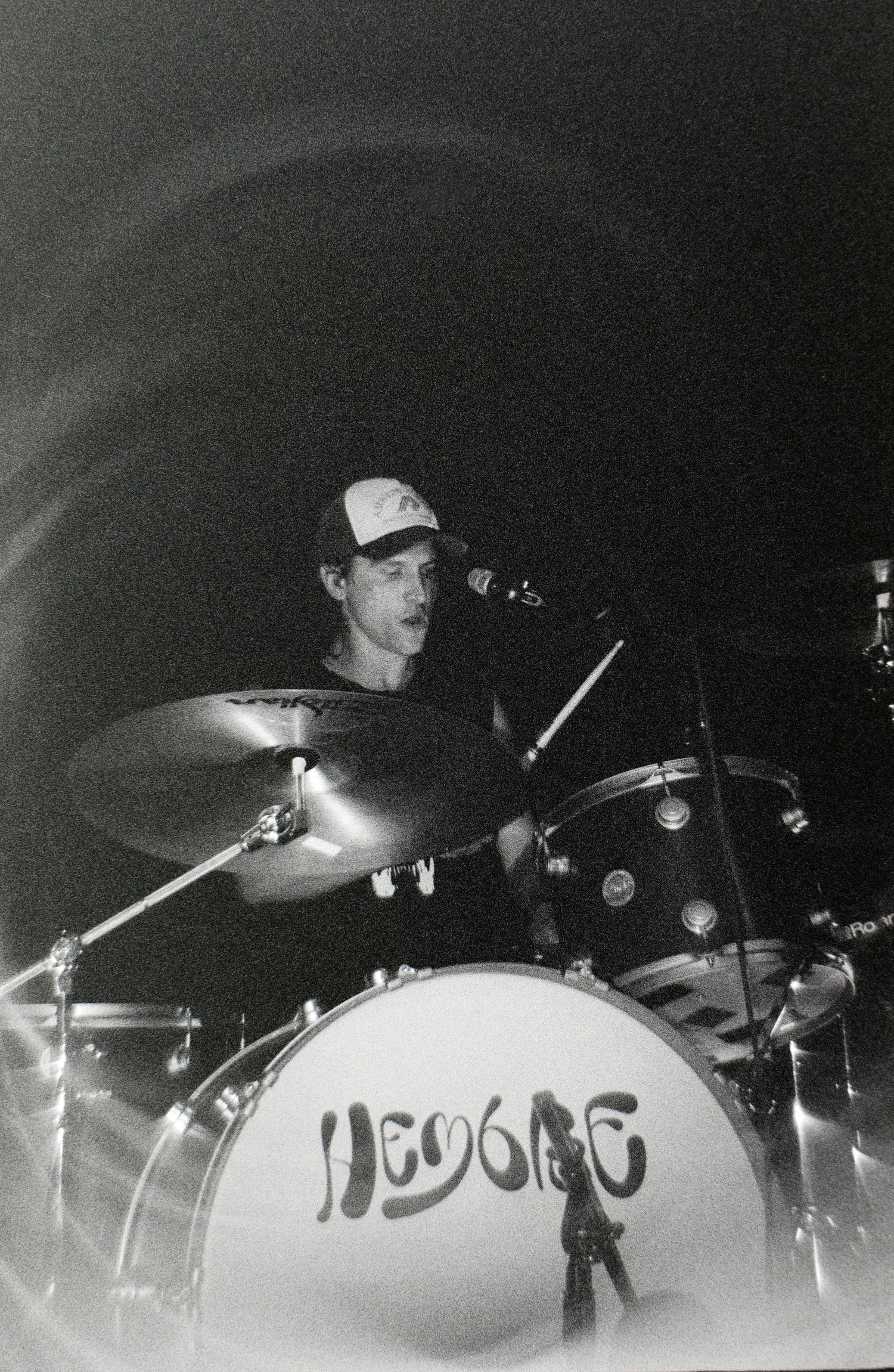 Black and white photo of a drummer performing on stage behind a kick drum labeled Hendrix at a live concert.