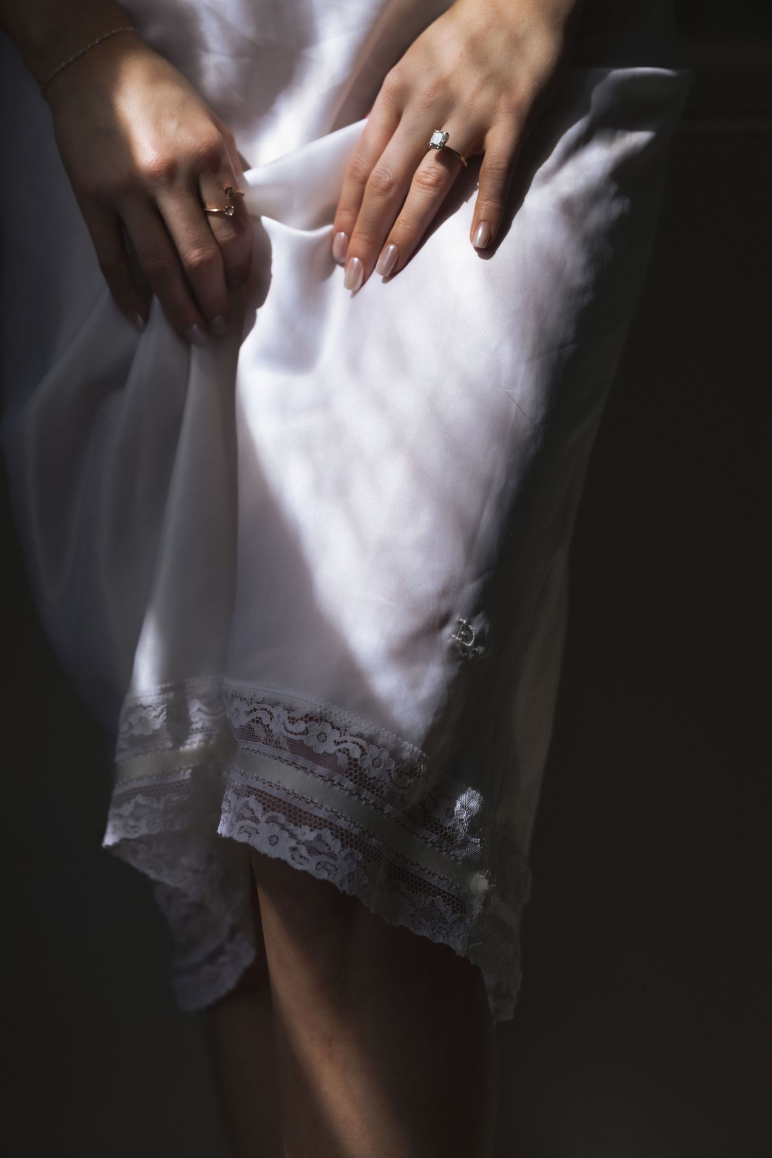 Woman in white lace-trimmed slip dress holding fabric, wearing elegant rings on both hands.