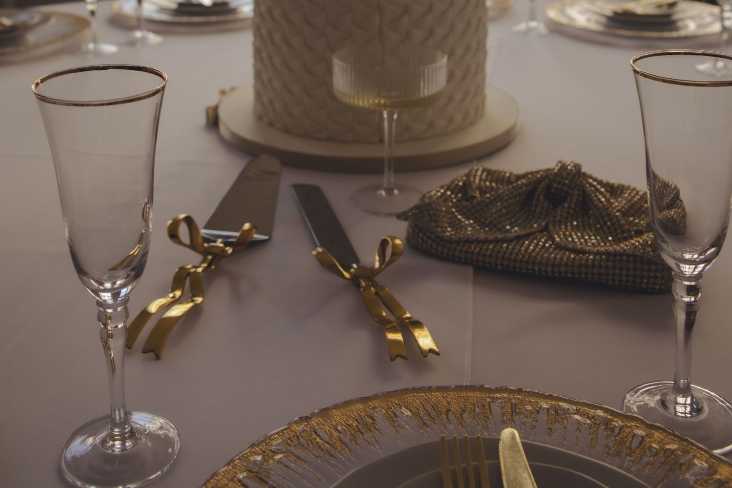 Elegant table setting with champagne flutes, golden cutlery, and ornate plates featuring gilded details and trim.