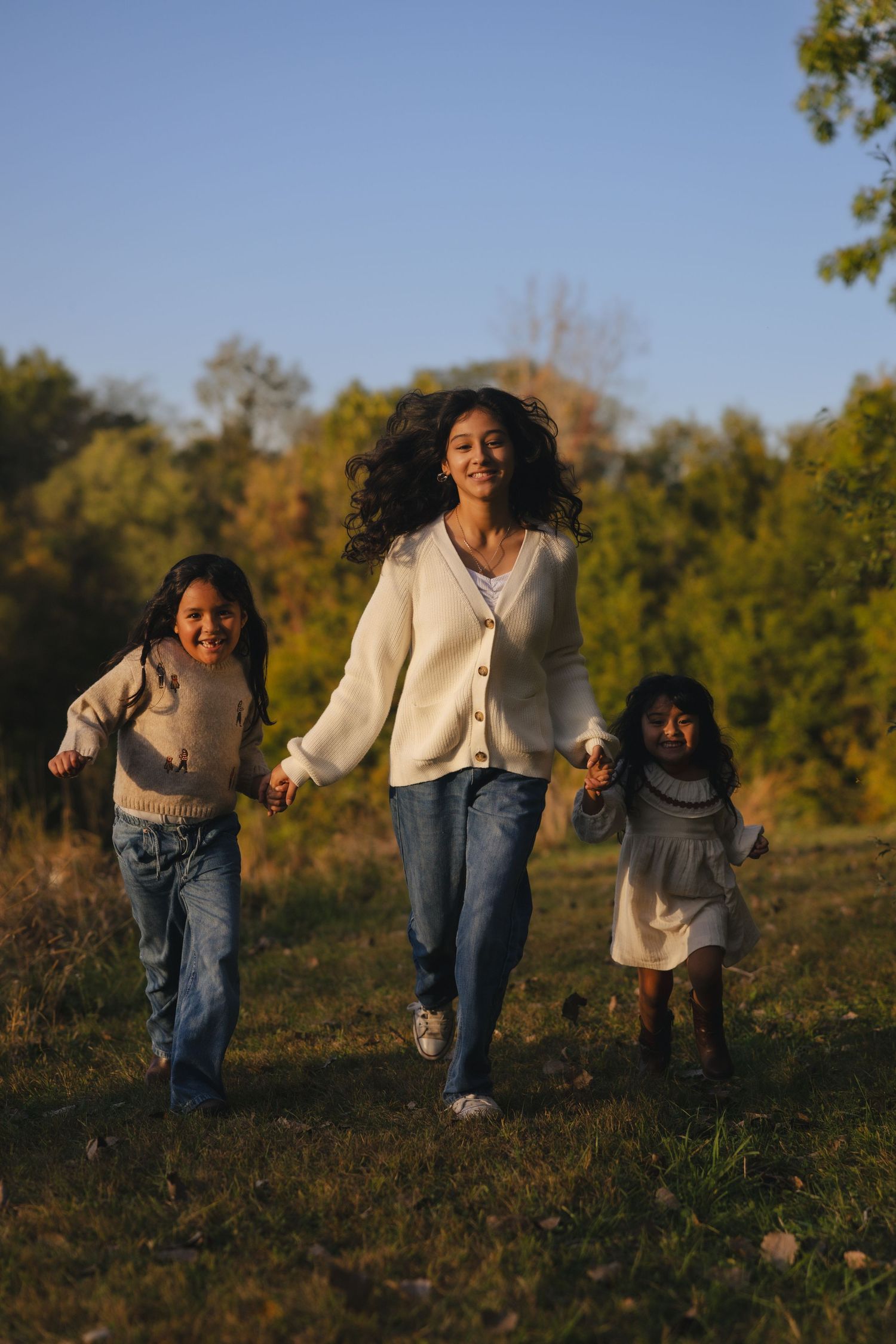 Three people run and play together on a grassy hill during golden hour on an autumn afternoon.