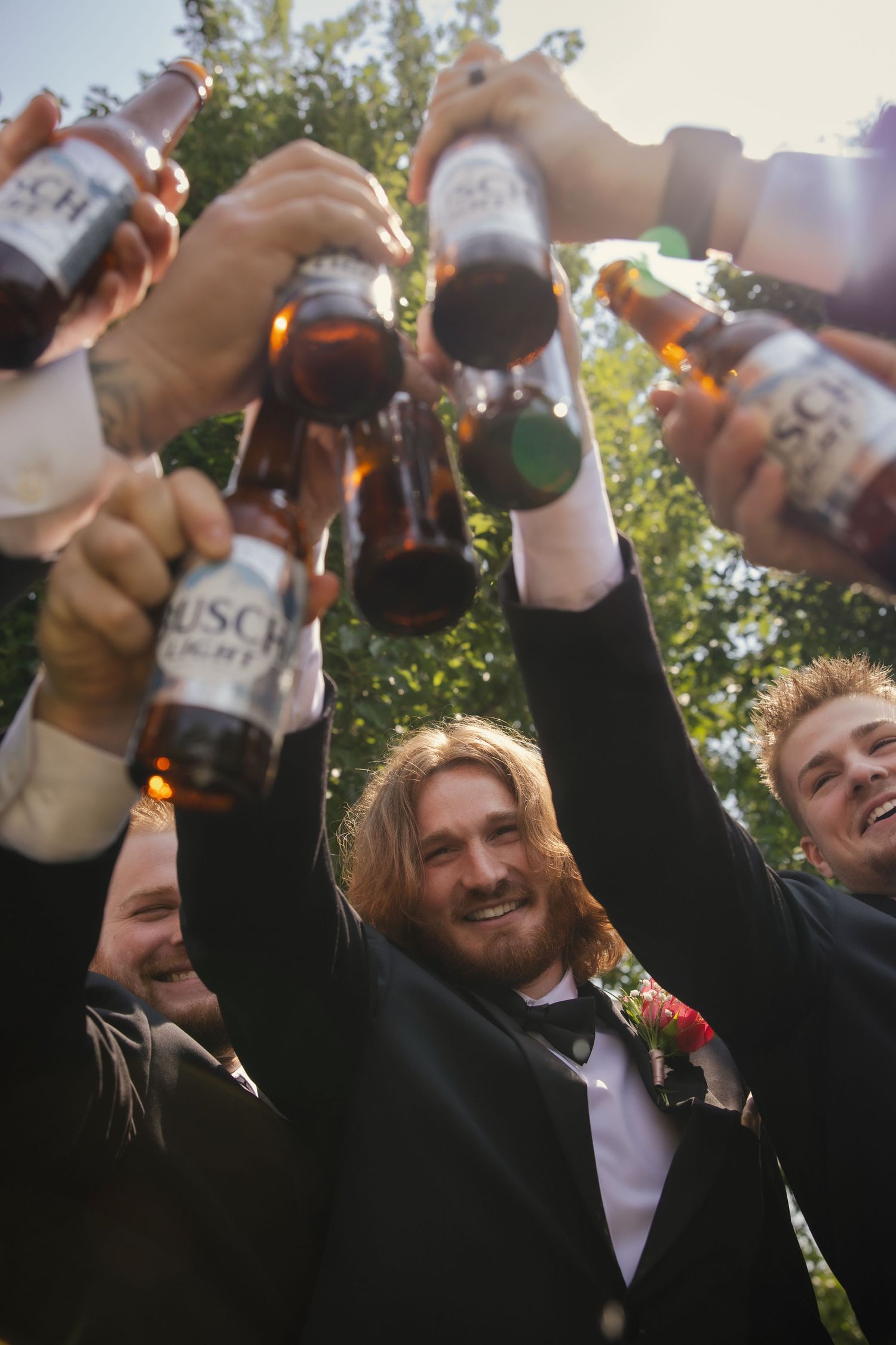A group of friends celebrating outdoors with raised beers in hand during a special occasion on a sunny day.