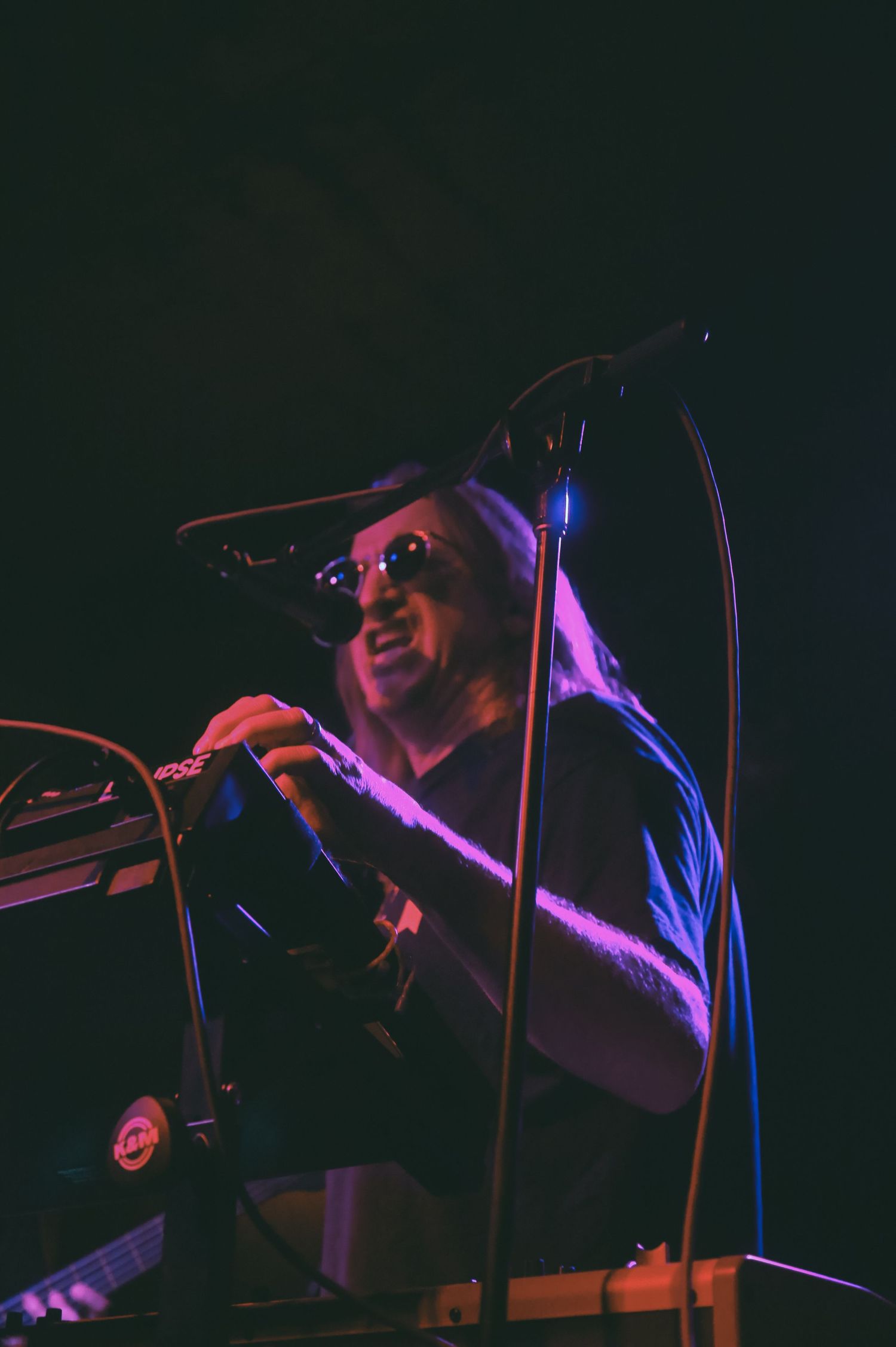 Musicians perform on stage at a dimly lit venue with dramatic purple and blue lighting effects creating an atmospheric mood.