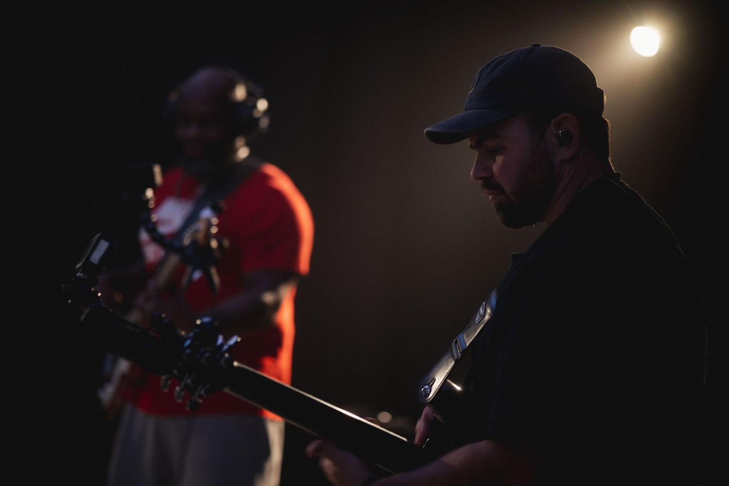 Two musicians play guitars in silhouette against dramatic stage lighting.