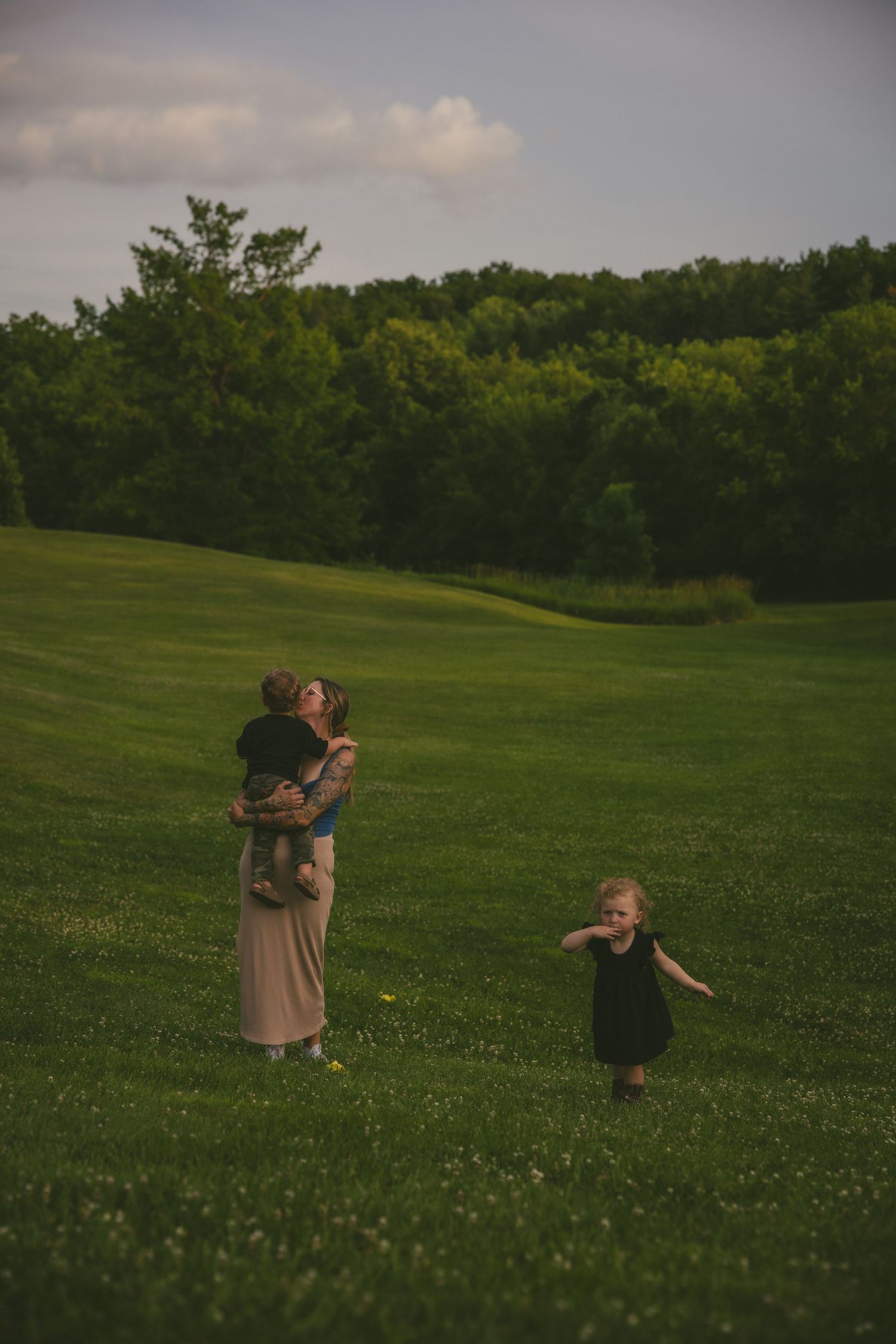 People stand together in a lush green field at dusk with forest trees in the background.
