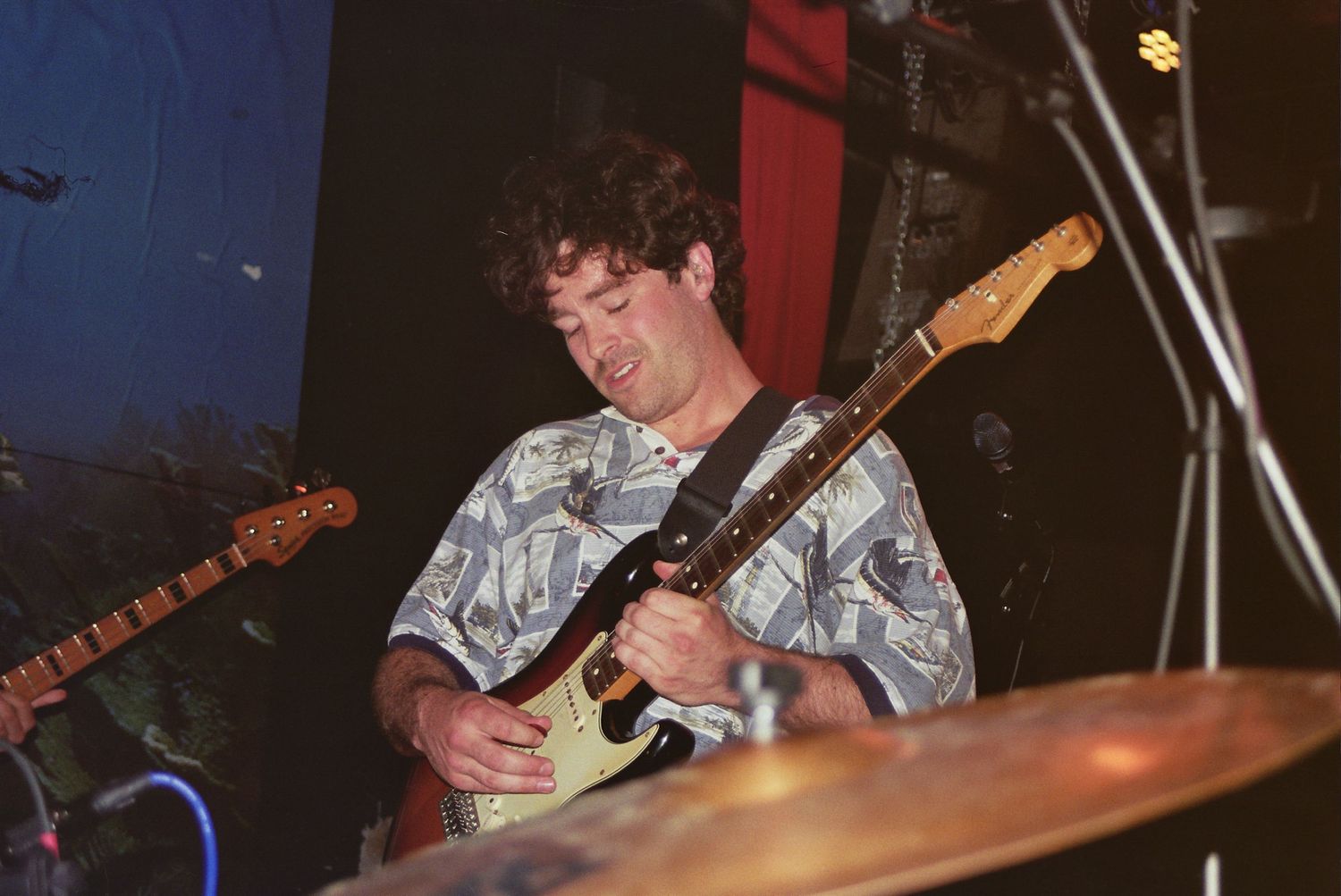Man playing electric guitar on stage under blue stage lighting at a live music performance.