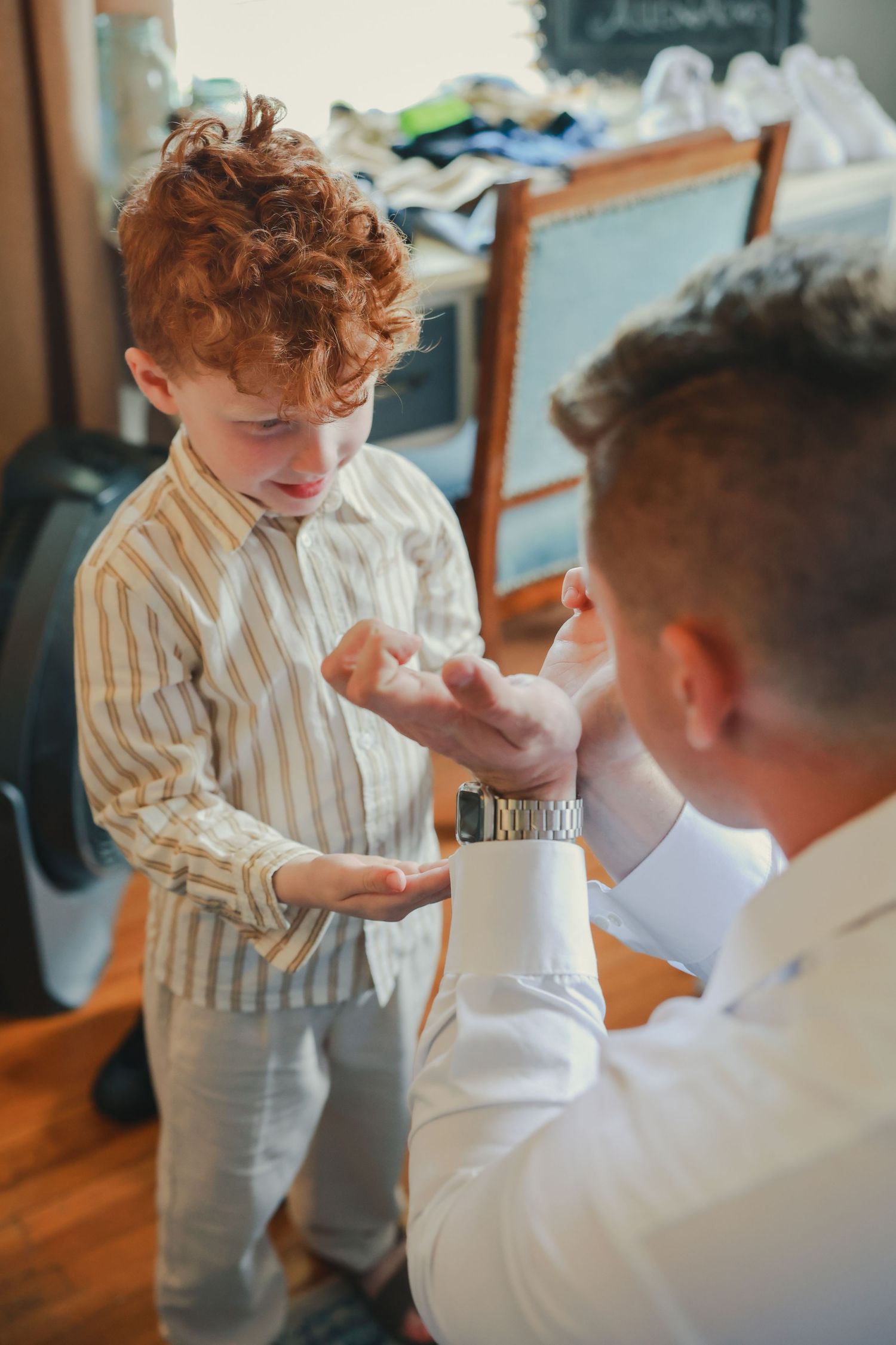 The person in white helps the young one wearing a striped shirt with putting on formal attire.
