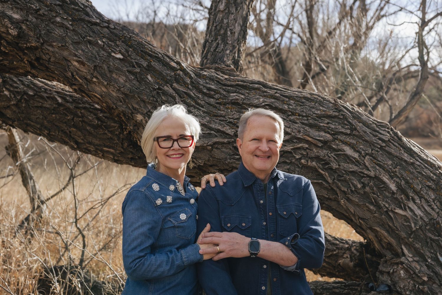 Two people sit together on a fallen tree trunk in a winter landscape during golden hour.