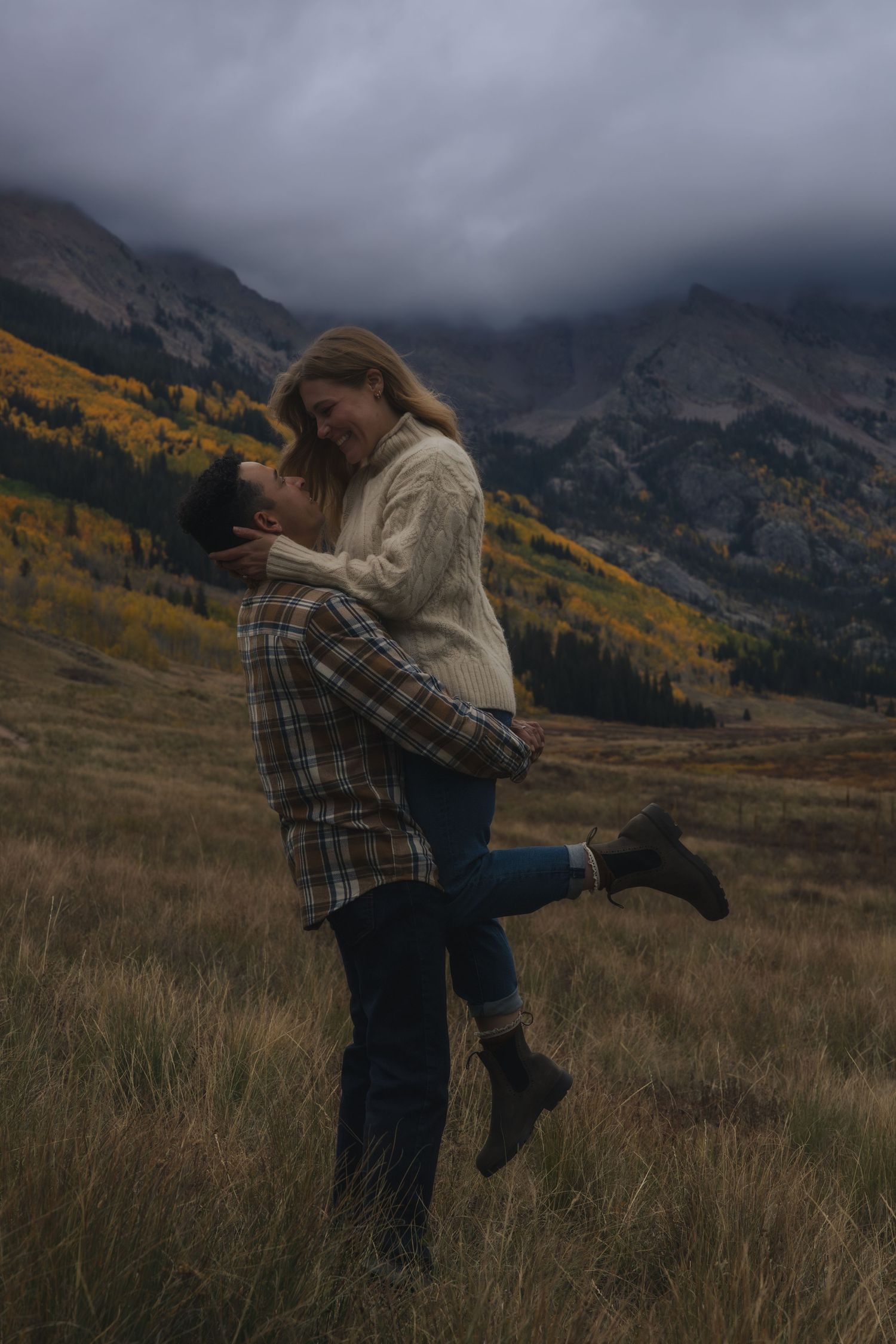 Couple embraces in a romantic moment against backdrop of misty mountain peaks and autumn foliage in Colorado.