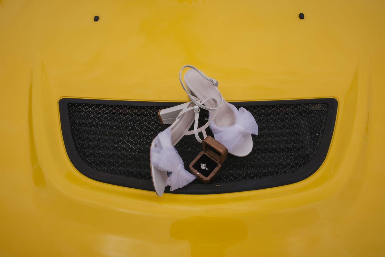 A white plastic duck decoration mounted on the black grille of a yellow vehicle.